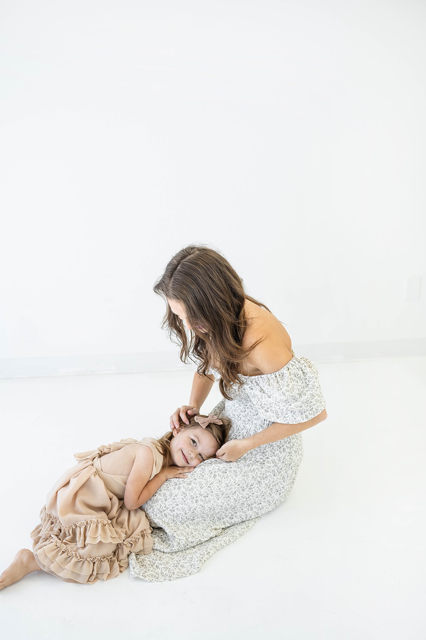 A young girl lays her head in the lap of her mother while sitting the the floor of a studio