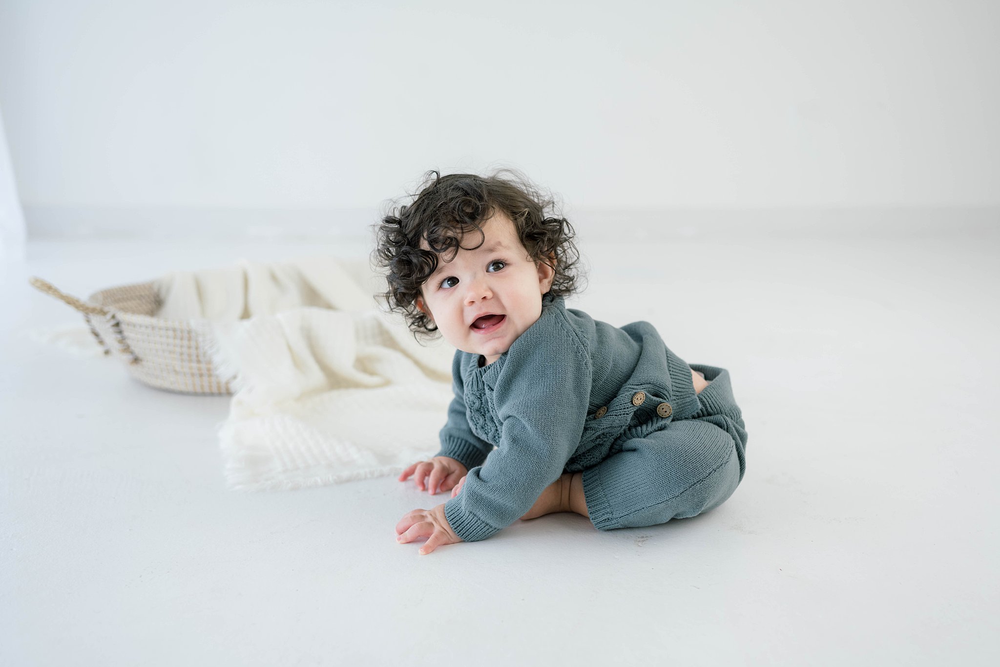 A young toddler in a blue outfit plays on the floor of a studio