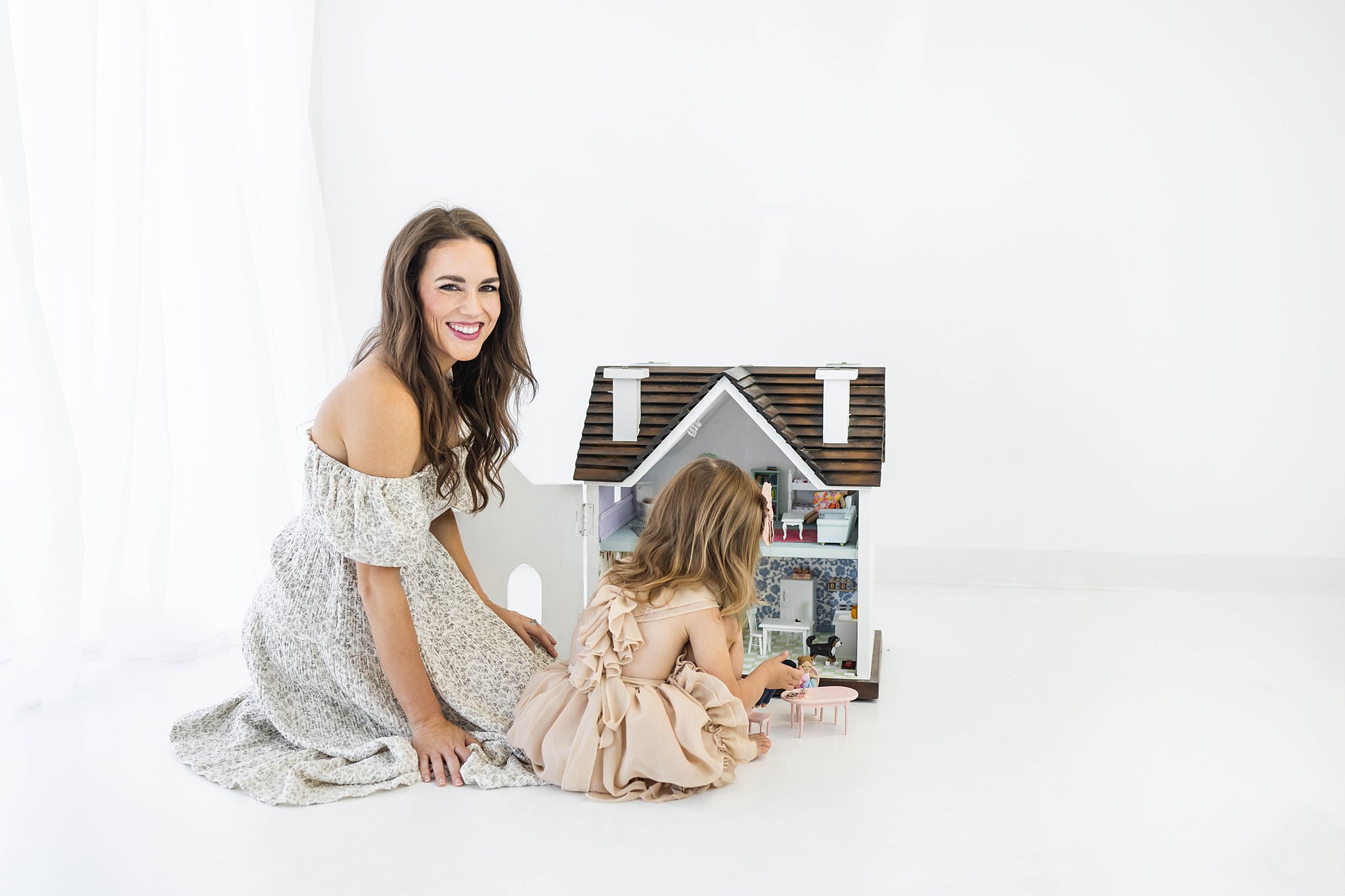 A mother and daughter sit on the floor of a studio while playing with a large dollhouse oklahoma city toy stores