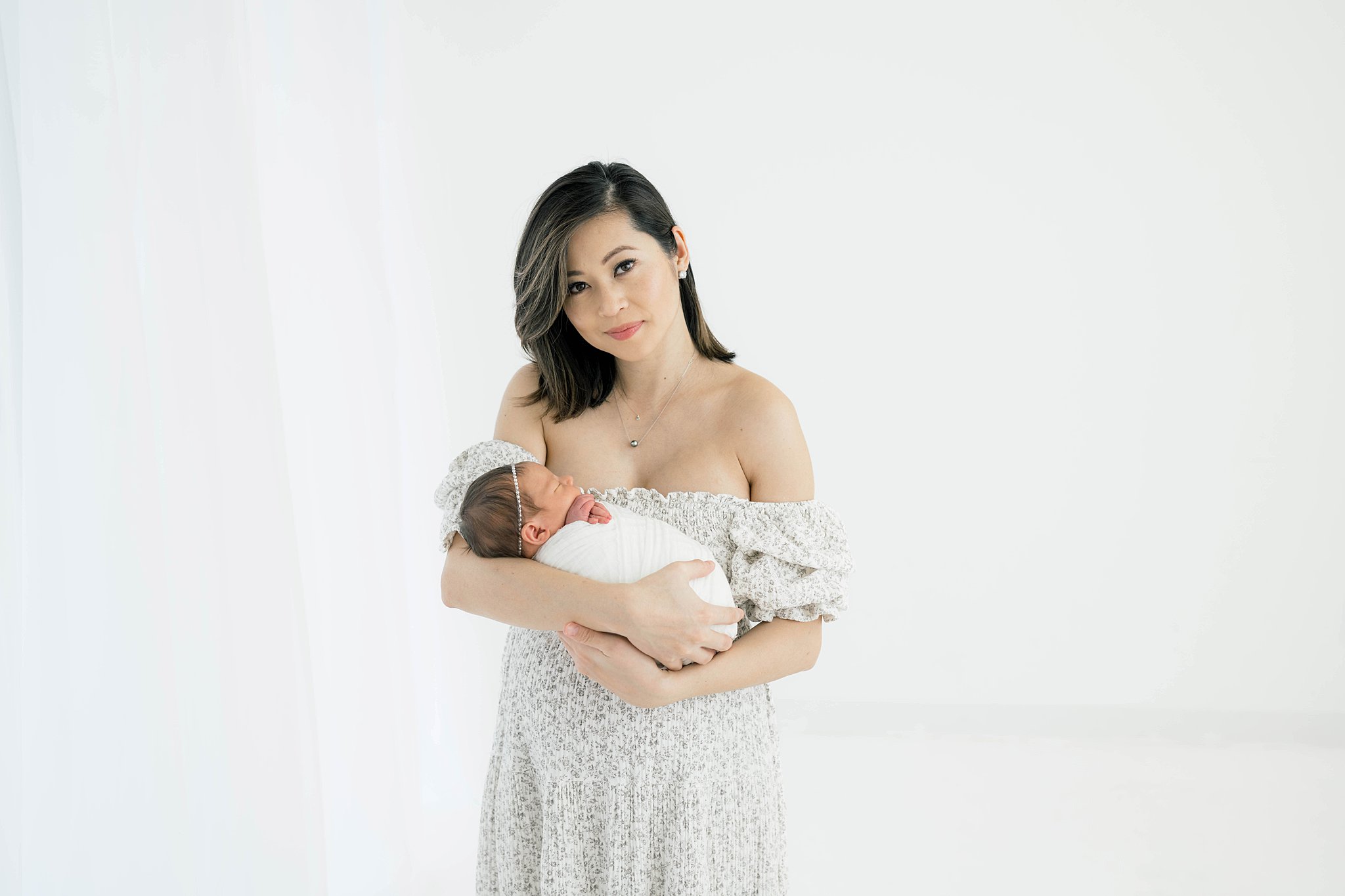 A mother in a floral dress with ruffle sleeves holds her newborn baby daughter in a studio pelvic floor therapy okc