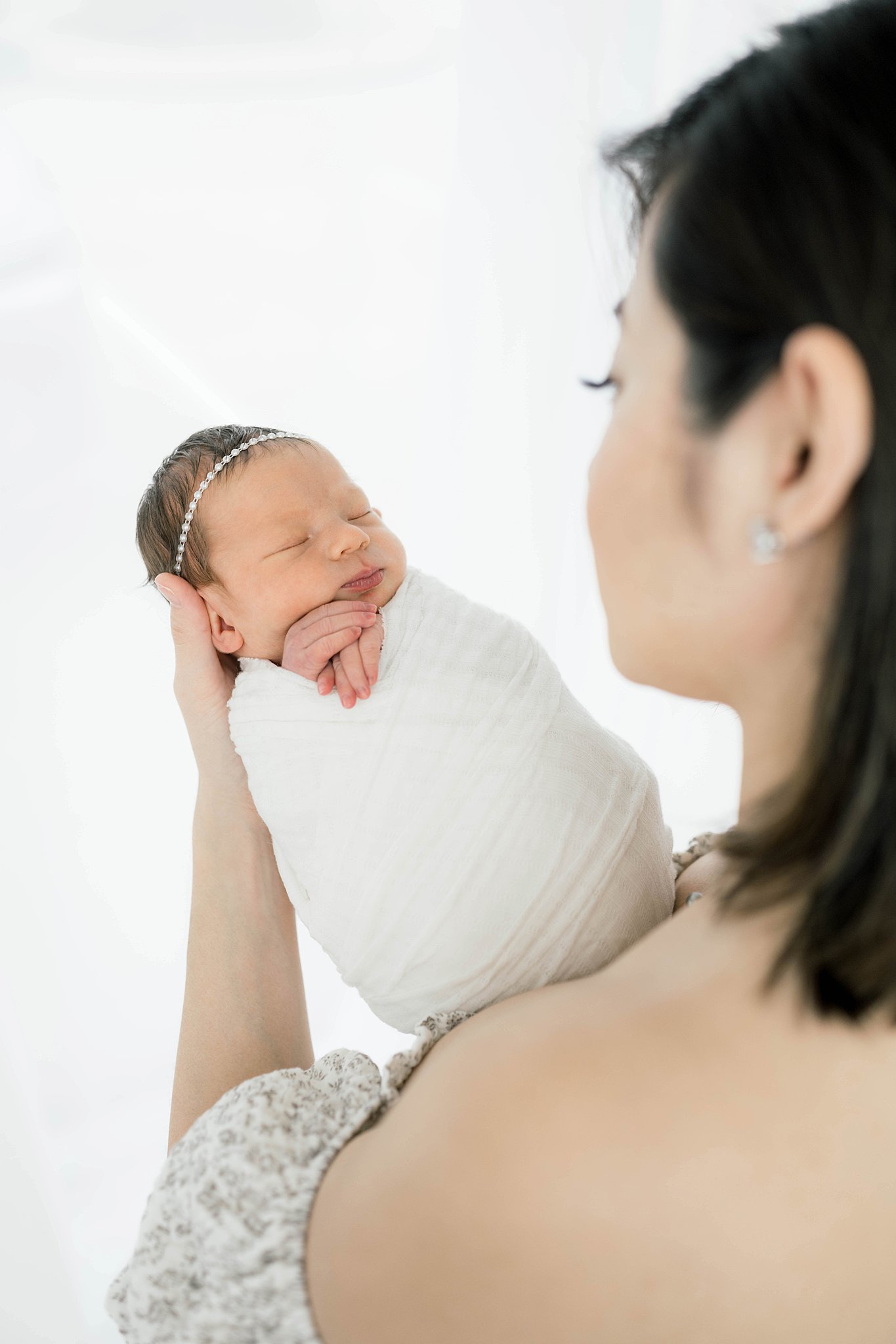 A mother holds her newborn baby girl while looking down at her in a studio