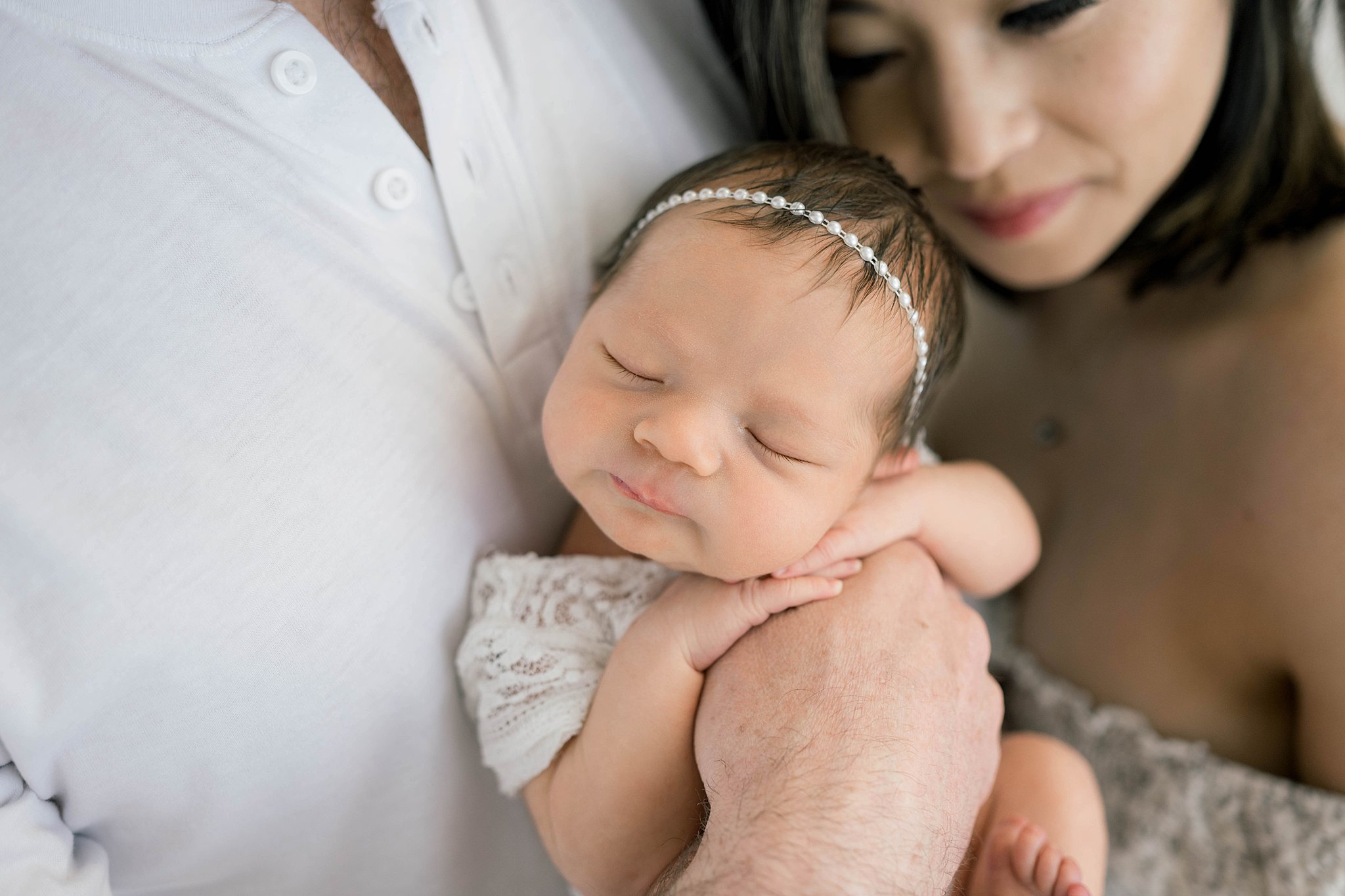 A newborn baby sleeps with her head on her hands while being held by dad with mom looking on prenatal yoga oklahoma city