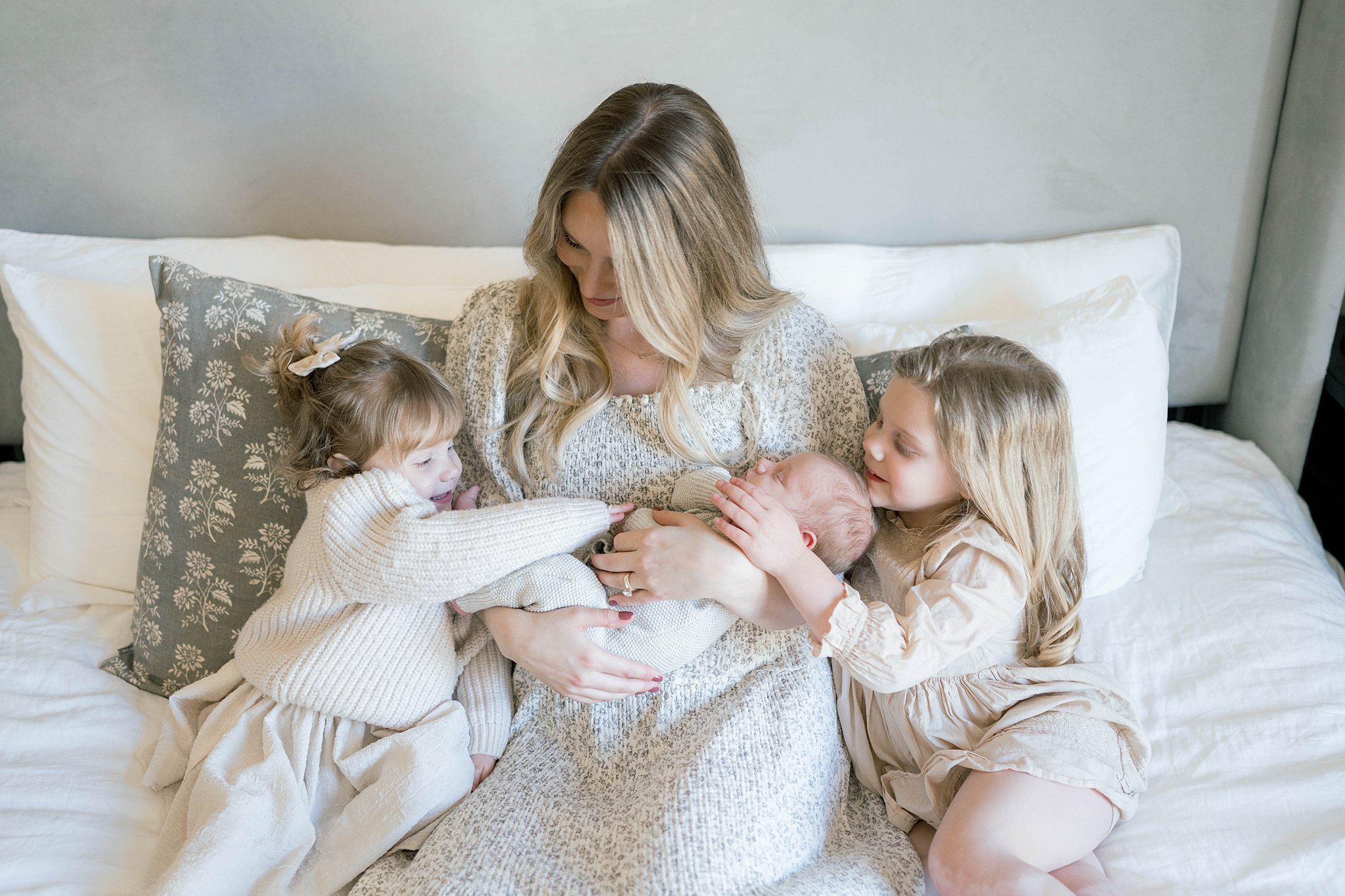 Two sisters play and gently touch their newborn sibling that is sleeping in mother's arms swaddle okc
