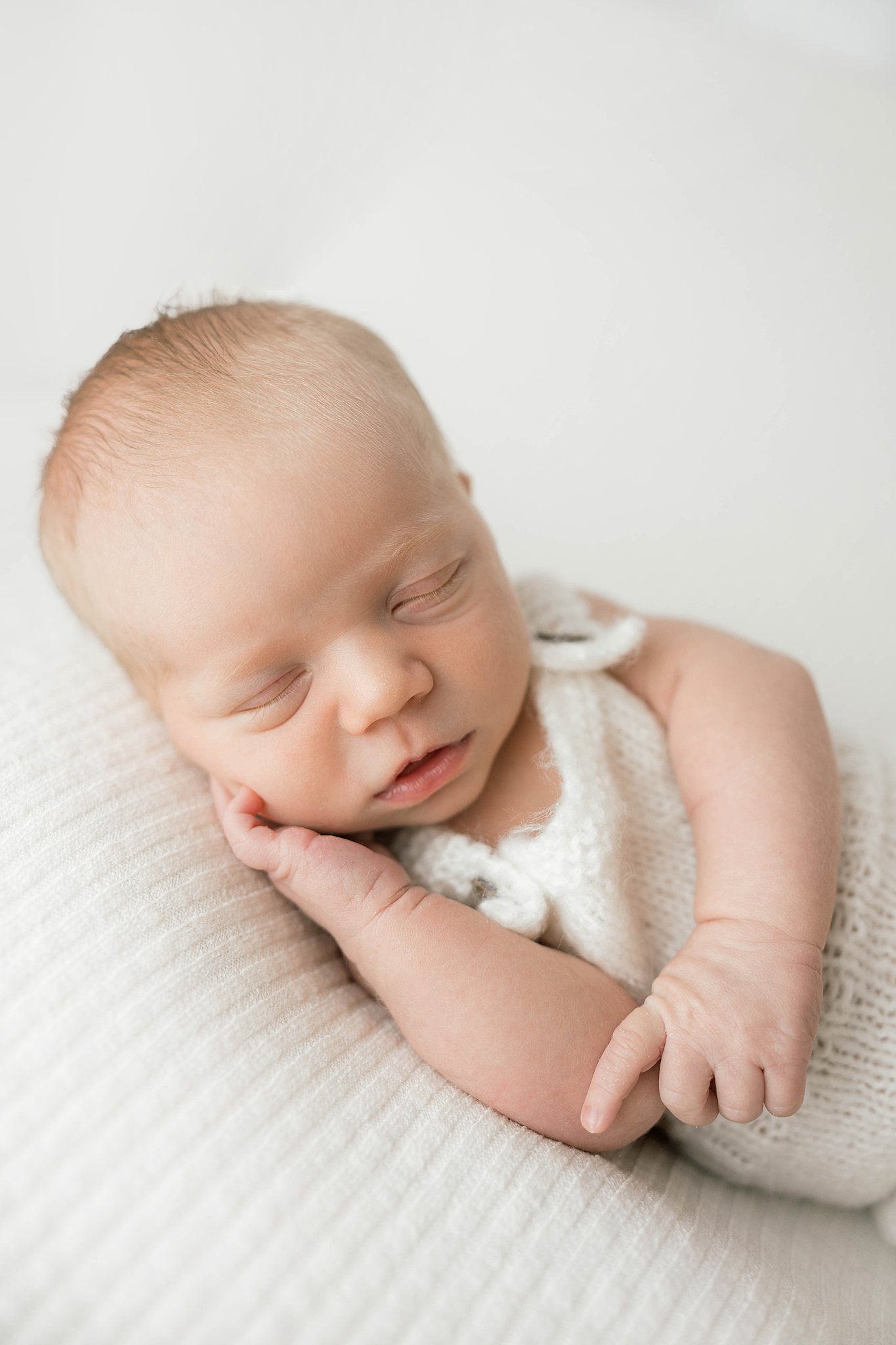 A newborn baby sleeps in a white onesie in a knit onesie isr swim lessons okc