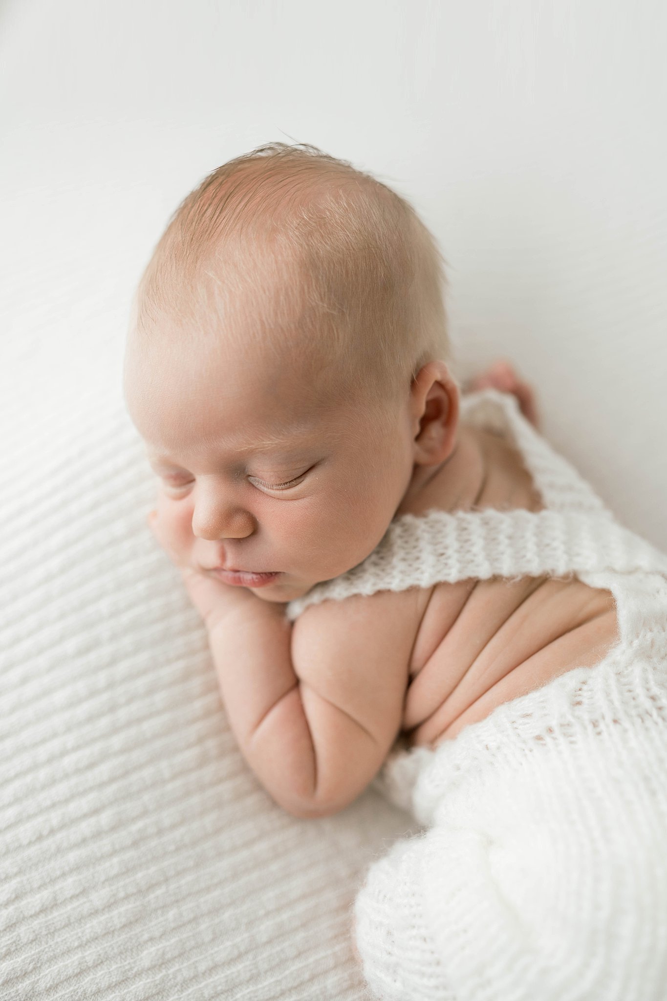 A newborn baby in knit overalls sleeps on its belly isr swim lessons okc