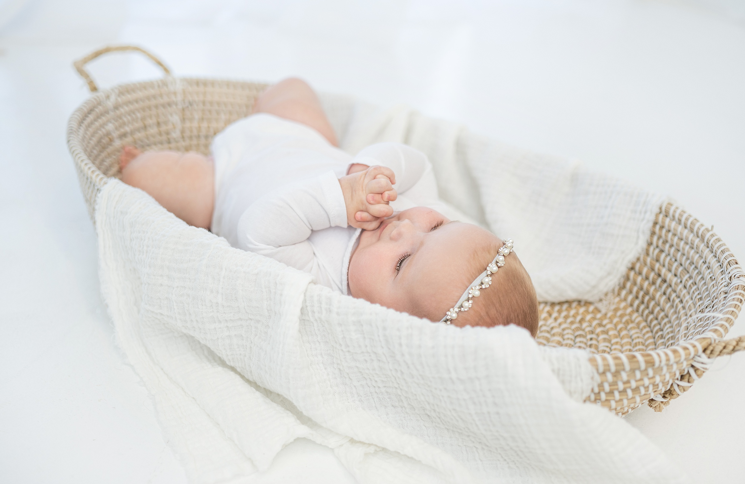 An infant lays in a woven basket wearing a white onesie