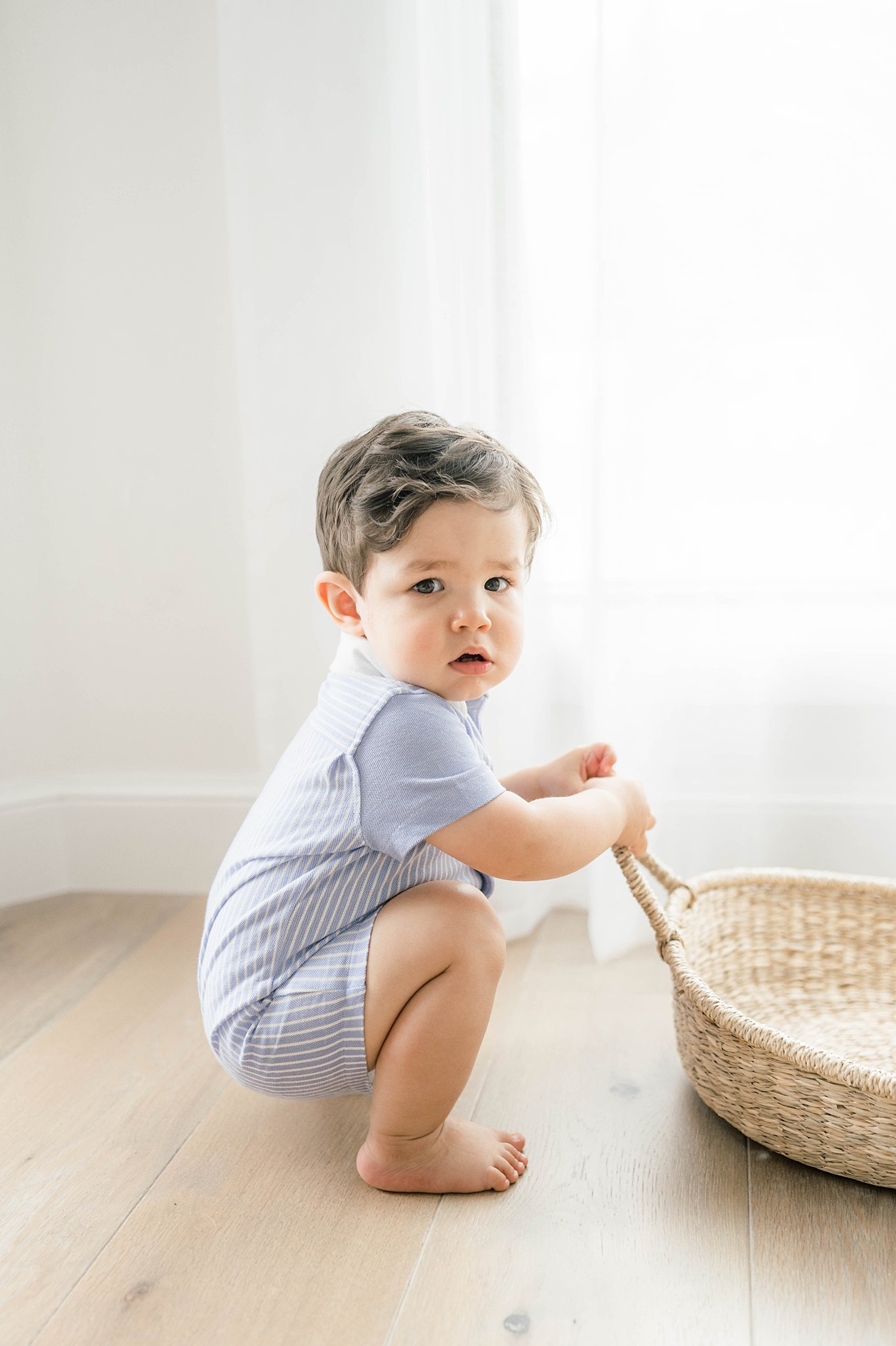 A young boy squats by a window while playing with a wicker basket okc family activities