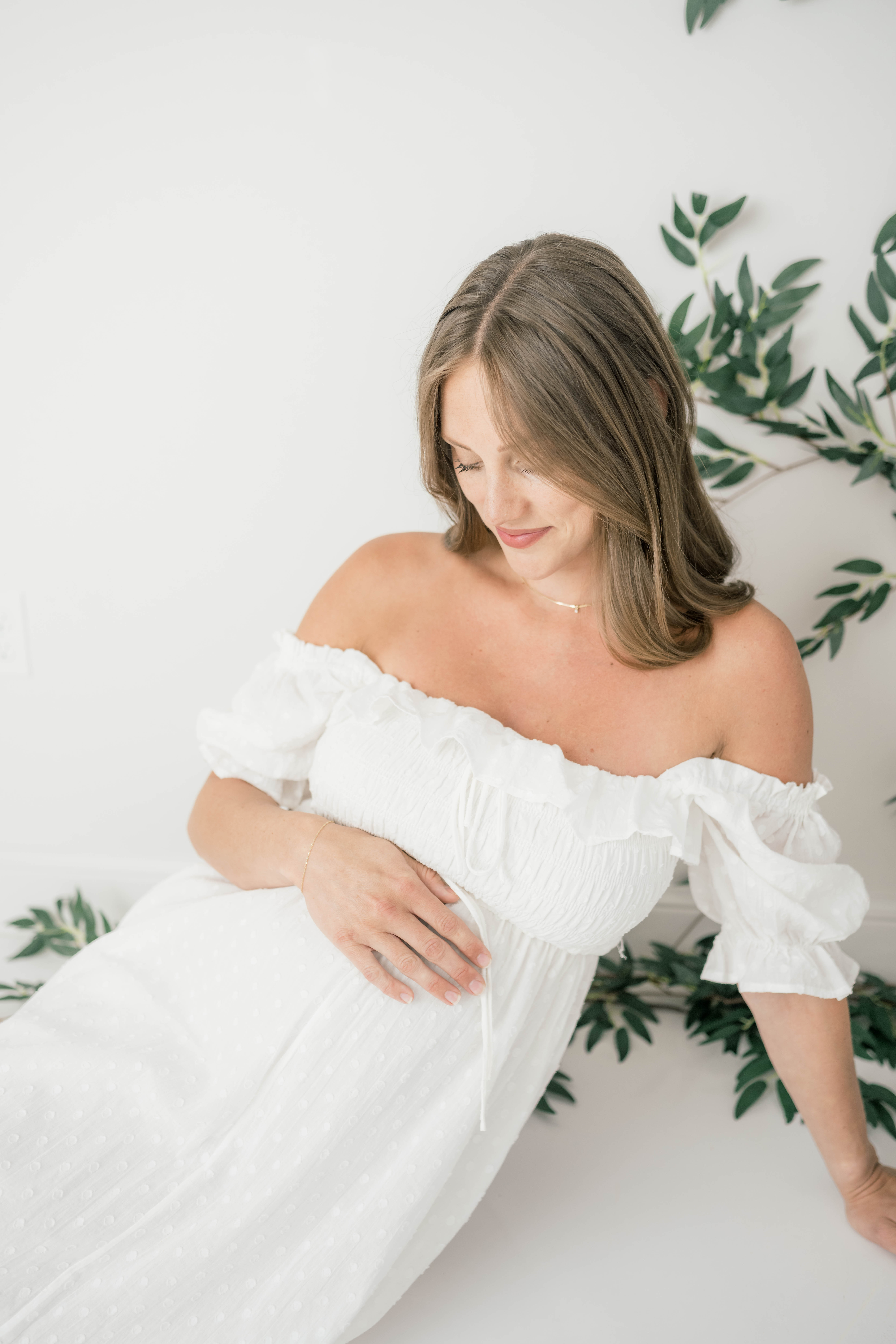 A mother to be lays across a studio floor in a white maternity gown the nest okc