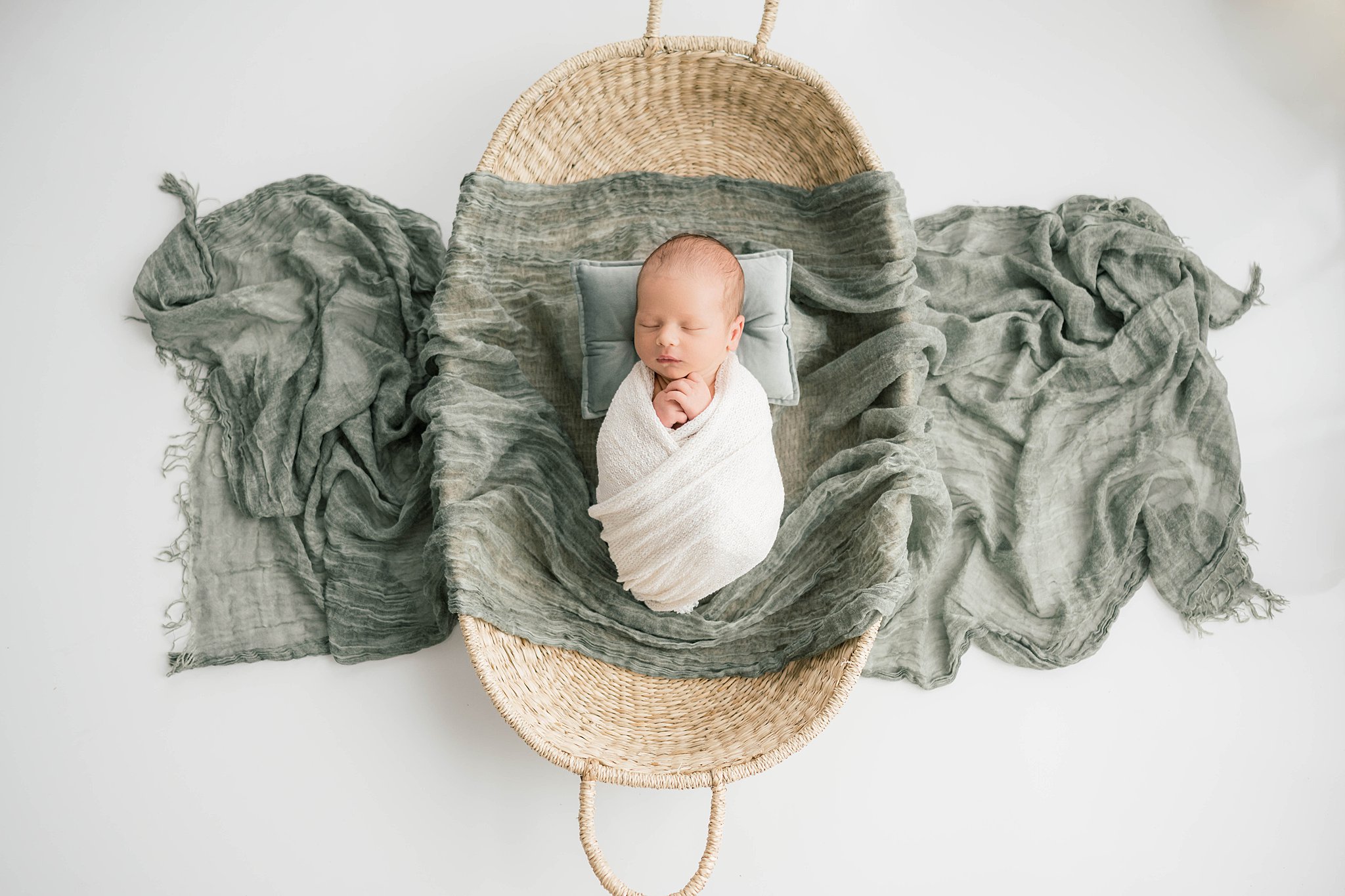 A newborn baby sleeps in a woven basket on a green pillow and blanket kidzone furniture