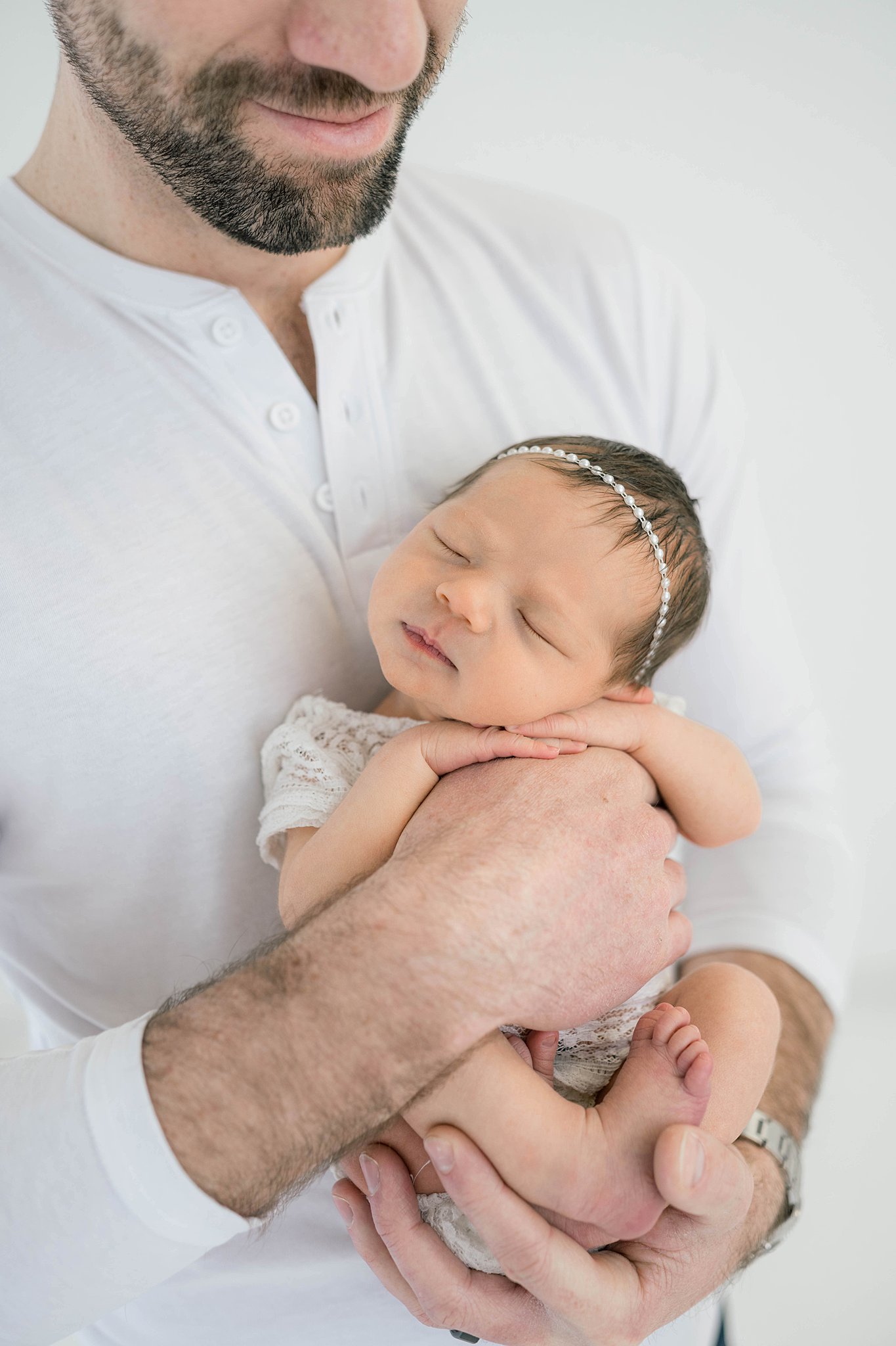 A new father holds his sleeping daughter against his chest while standing in a studio okie babies