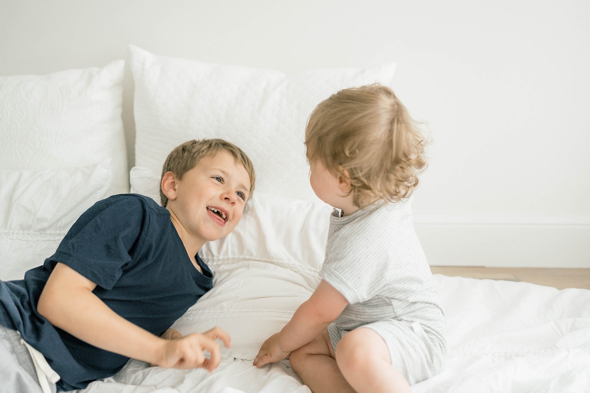 Two young boys play together on a white bed in a studio unpluggits okc
