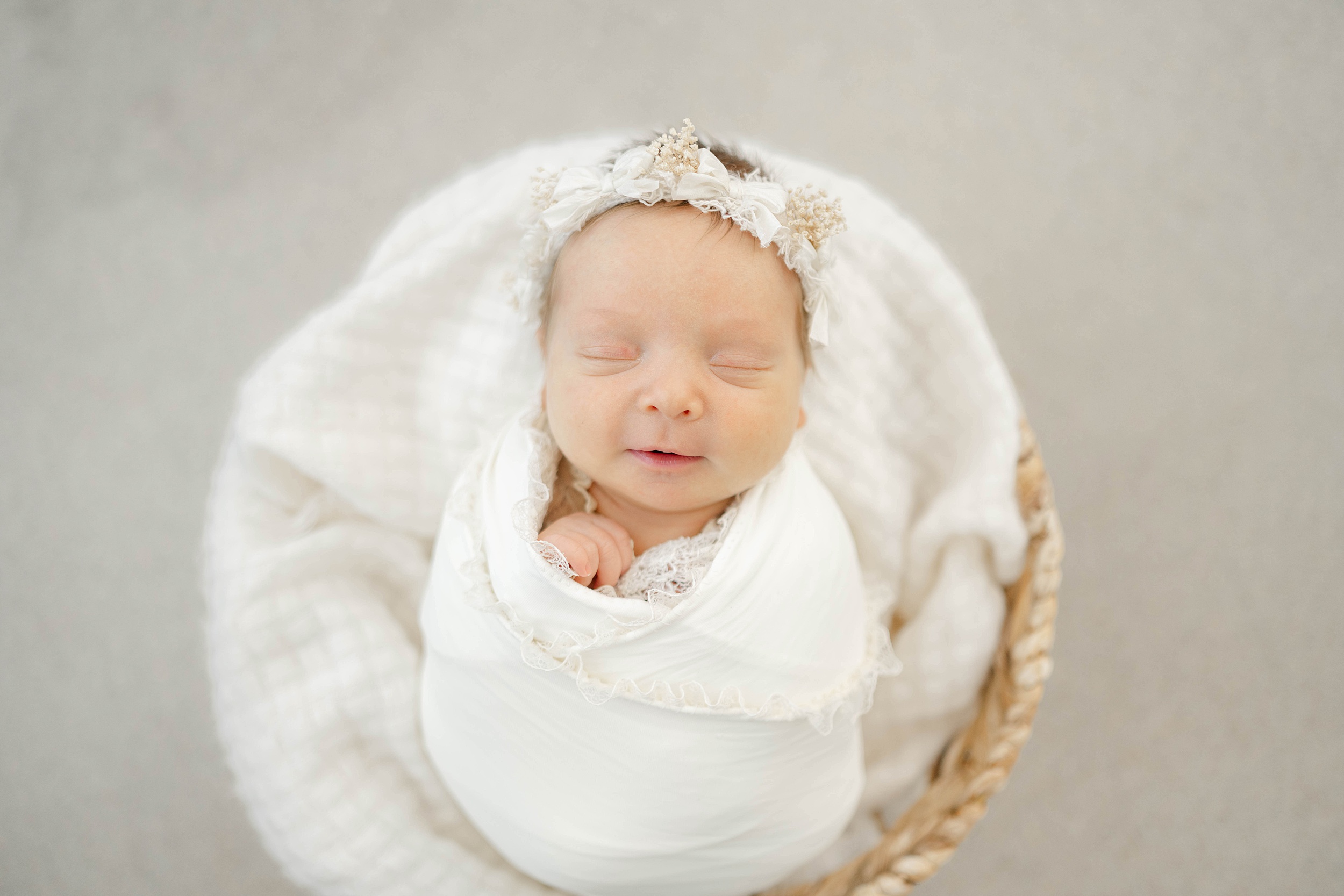 A newborn baby girl sleeps in a white swaddle in a woven basket