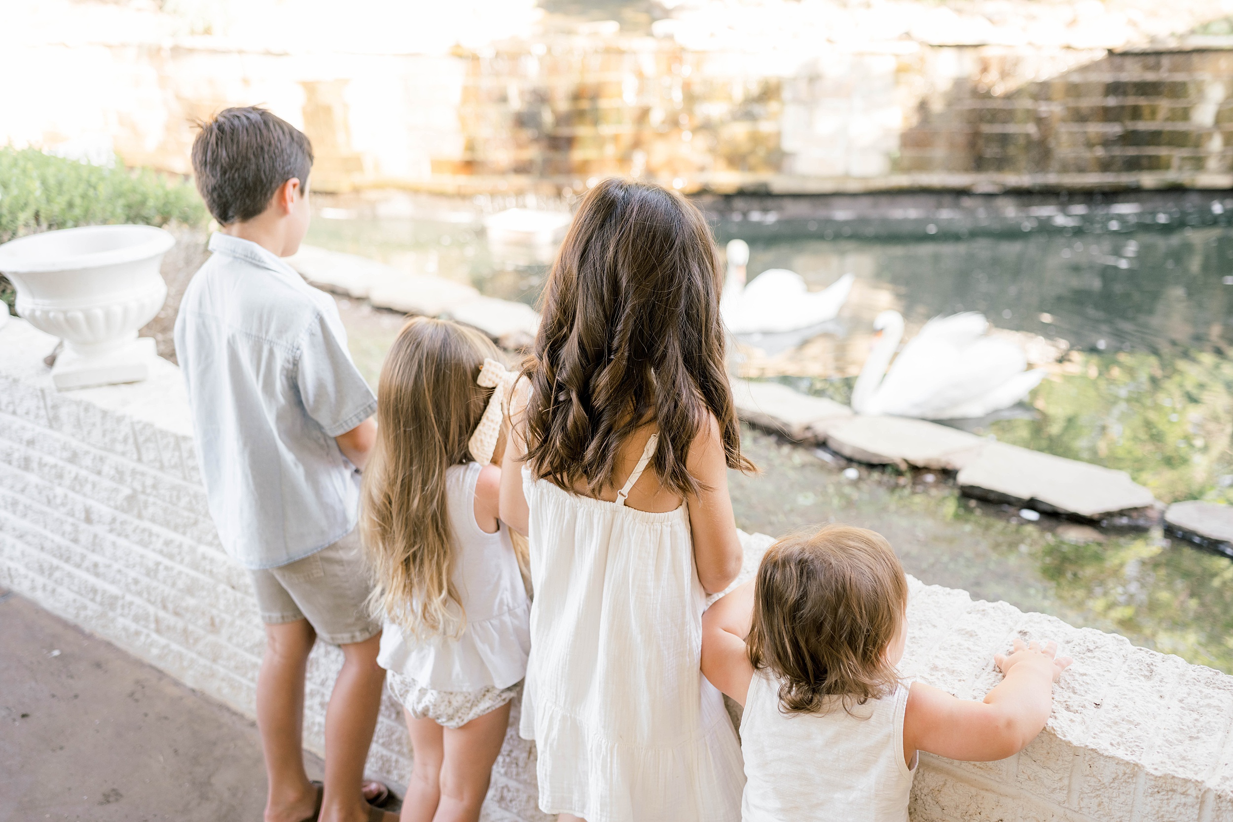 Four young siblings stand on against a wall overlooking swans in a pond before visiting kid friendly restaurants okc