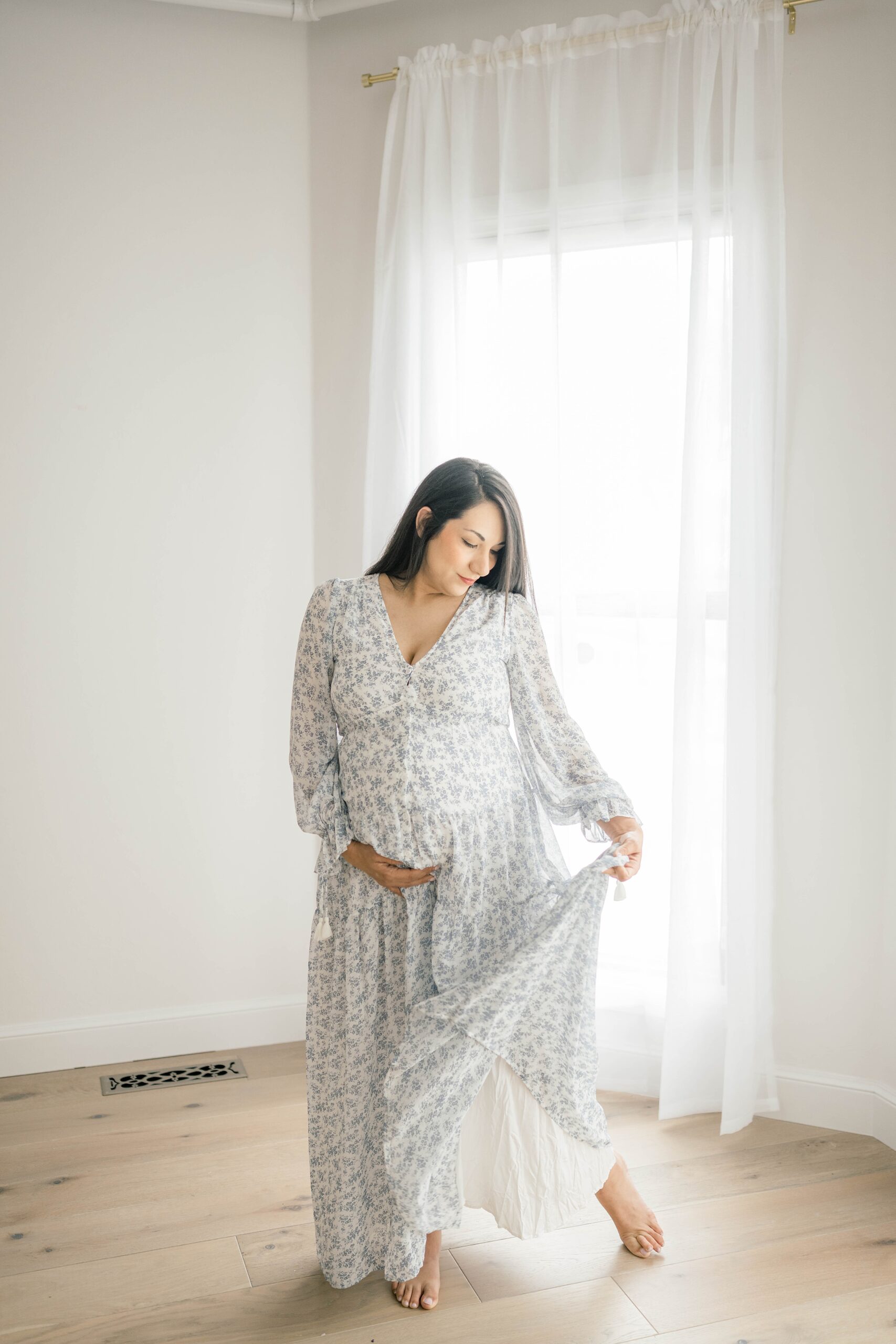 A mom to be walks through a studio playing with her floral print dress and holding the bump thanks to oklahoma city fertility clinic