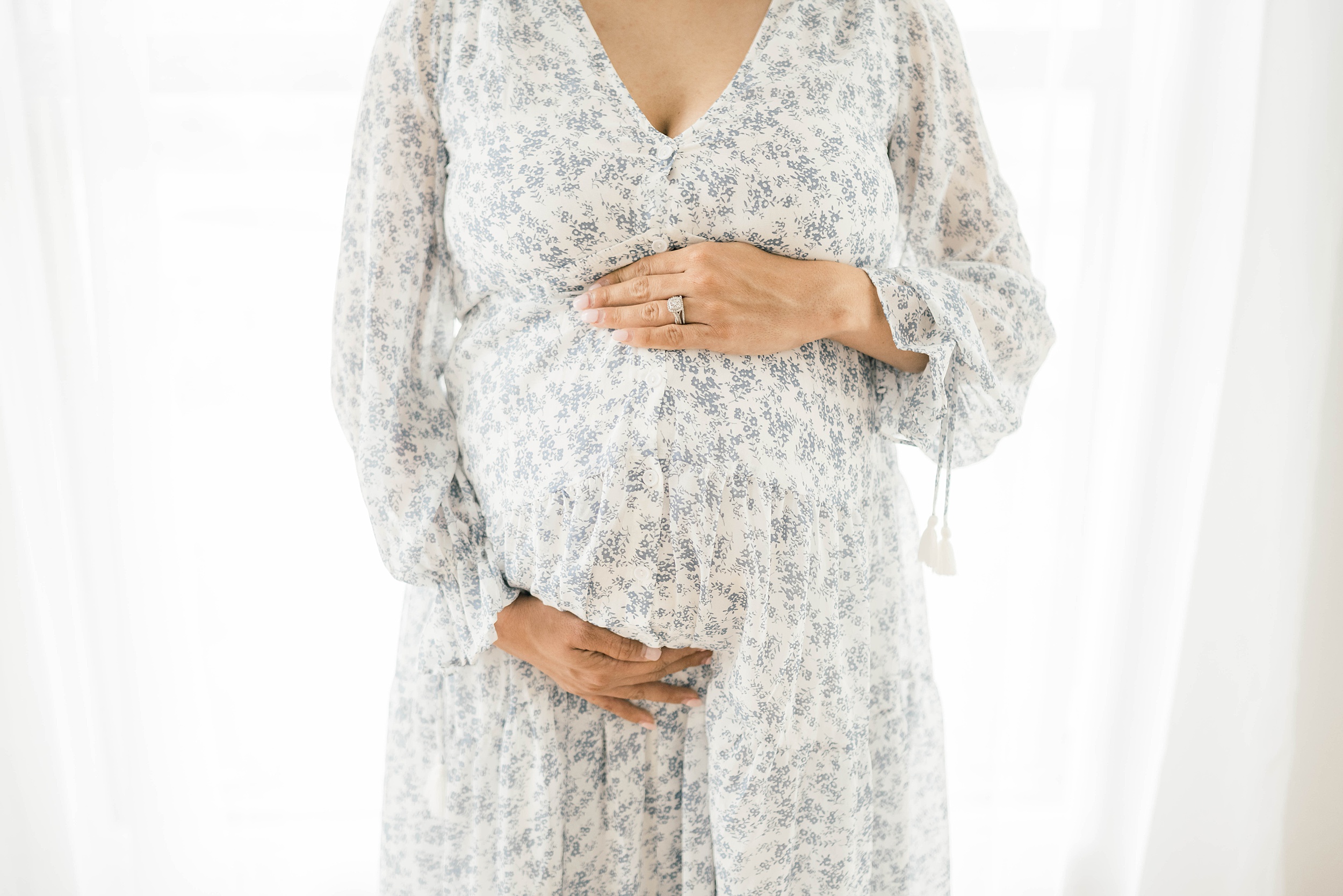 Details of a mother to be in a floral print dress holding her bump in a studio thanks to oklahoma city fertility clinic