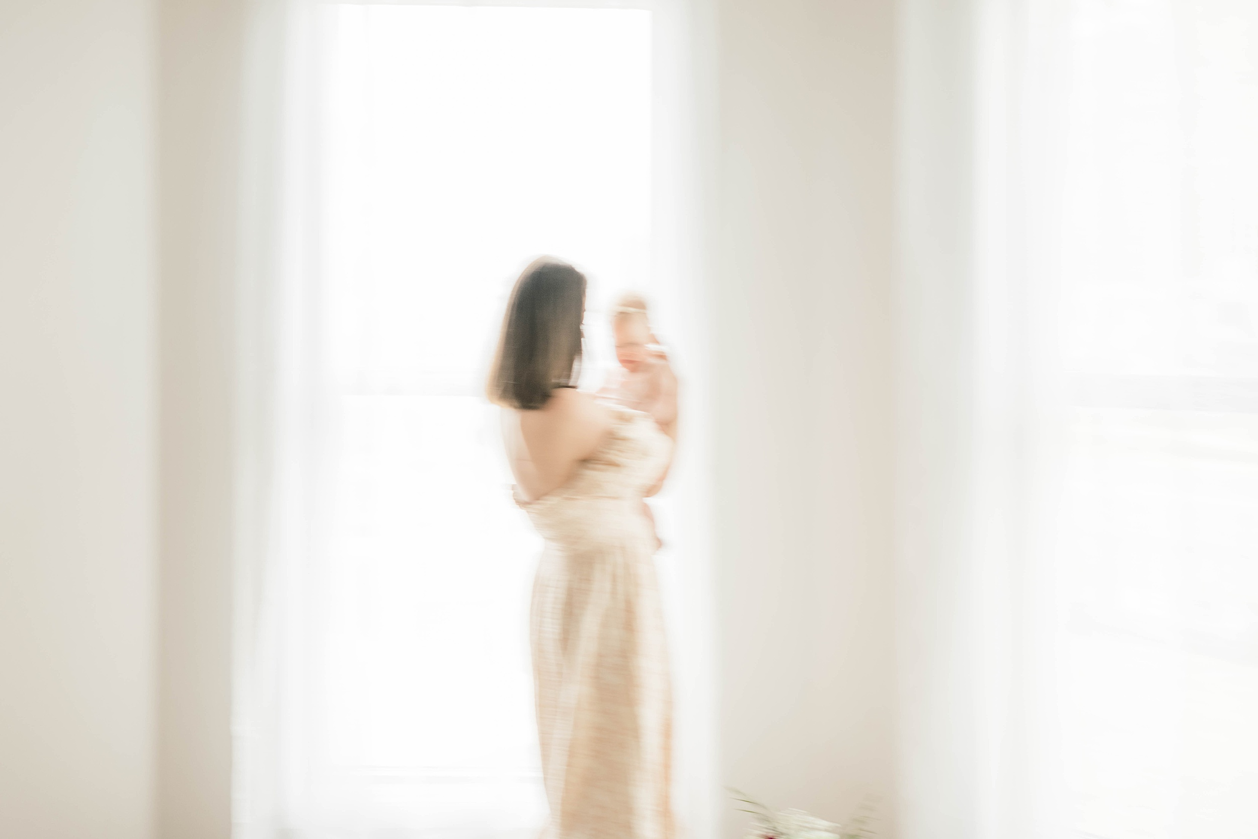 A Mother stands in a window holding her newborn baby in a studio