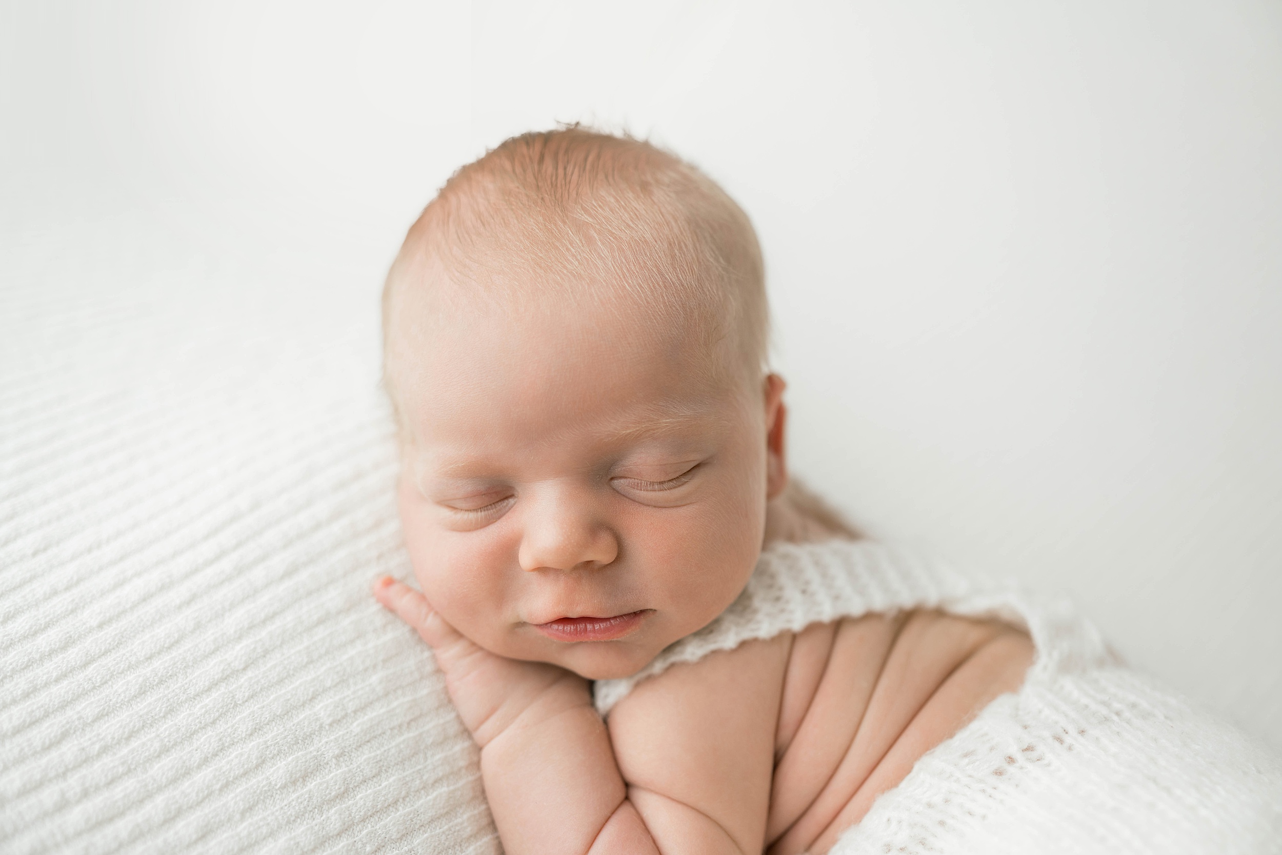 A newborn baby sleeps in knit overalls on a white bed in a studio thanks to ou children's hospital