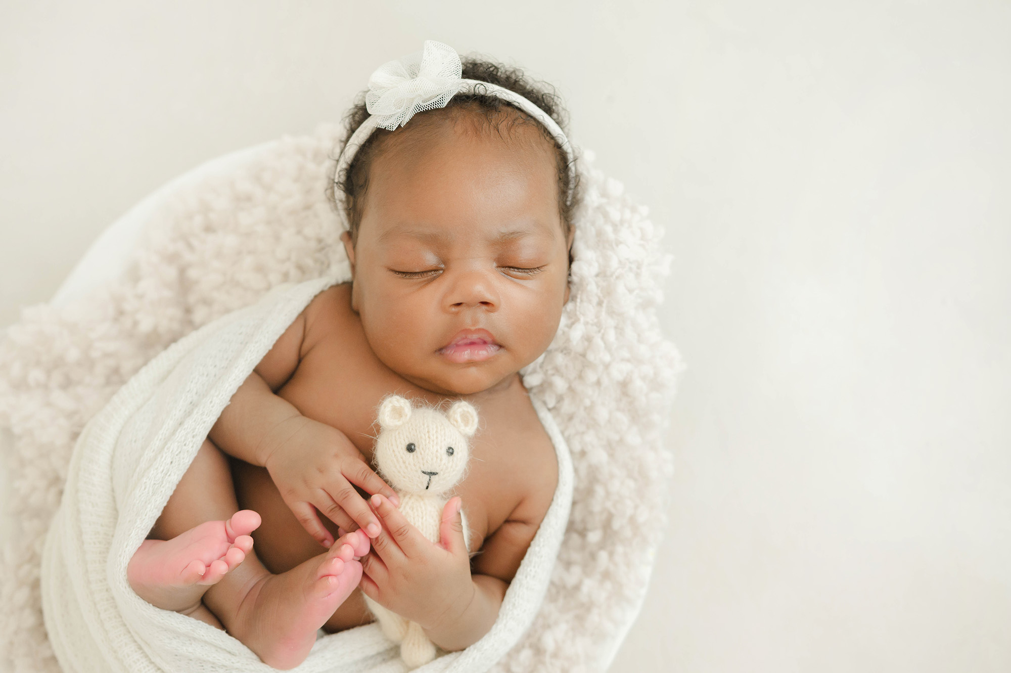 A newborn baby sleeps in a swaddle holding a white knit bear after meeting an au pair in oklahoma city