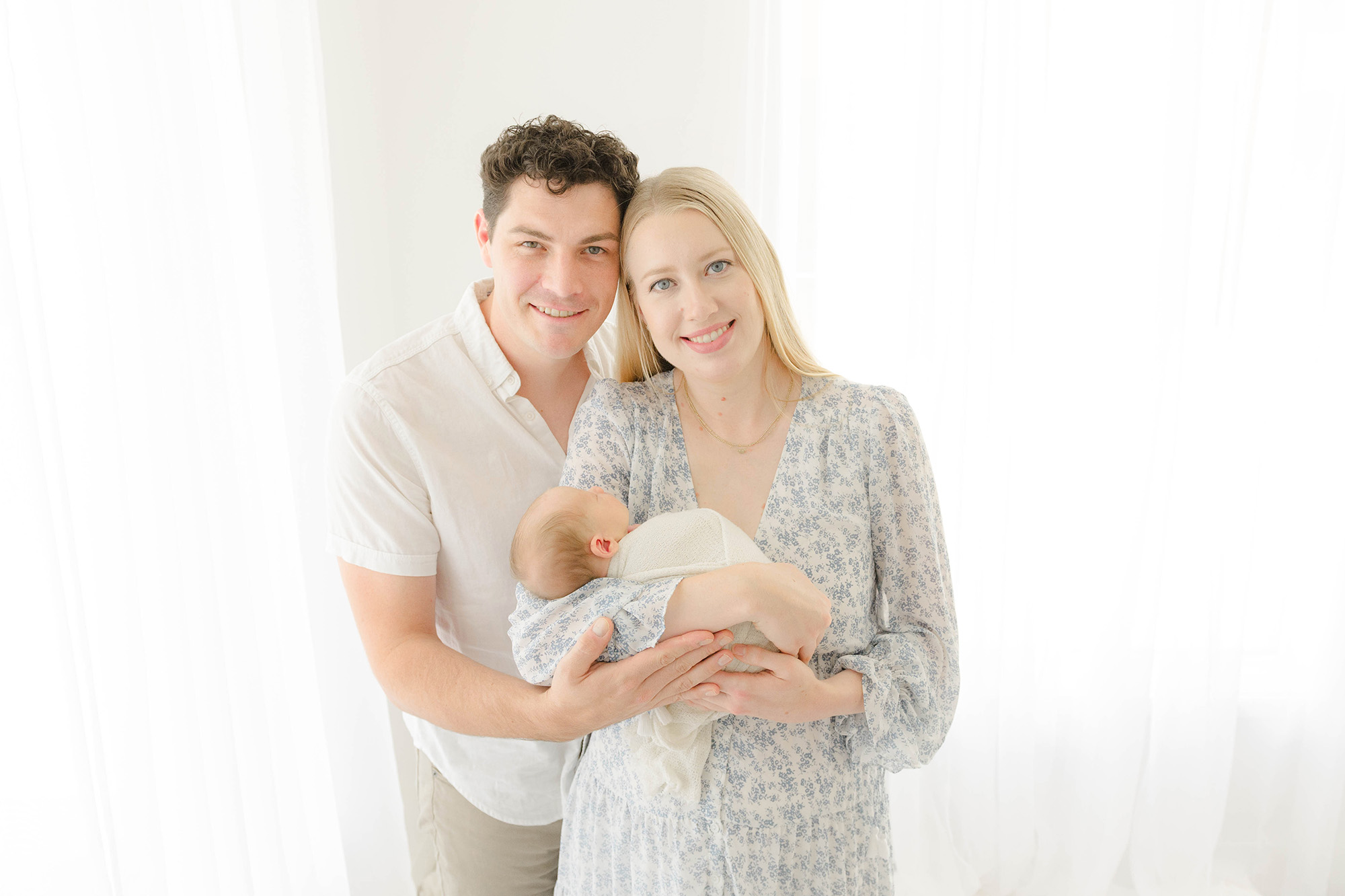 Happy new parents stand touching heads with their newborn baby in mom's arms after visiting baby boutiques in okc