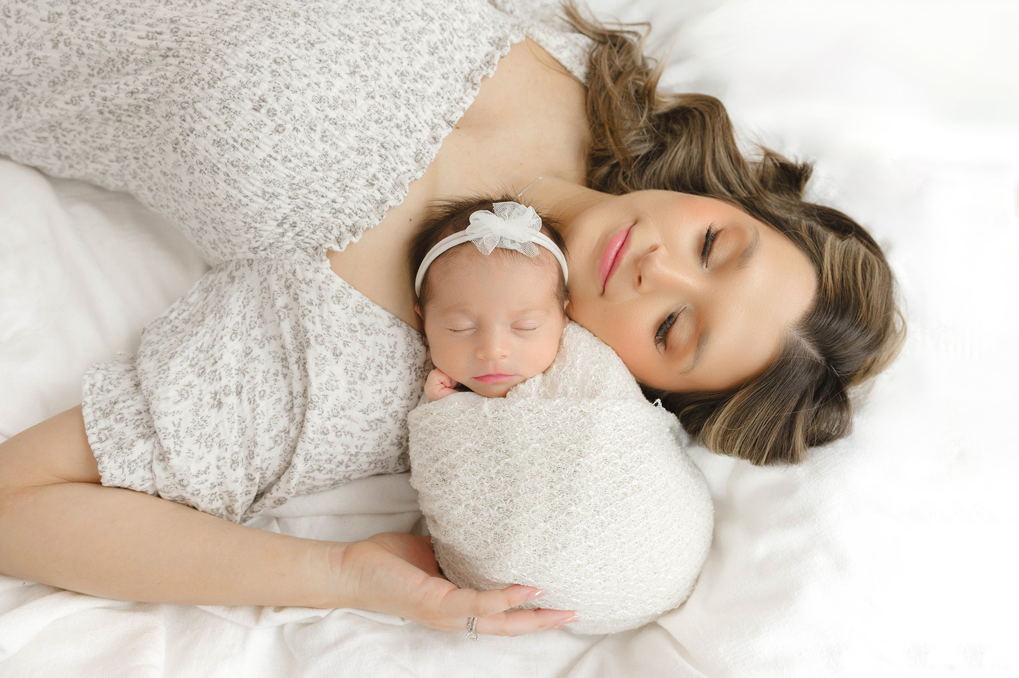 A happy new mom sleeps on a bed with her newborn sleeping on her shoulder after meeting babysitters in okc