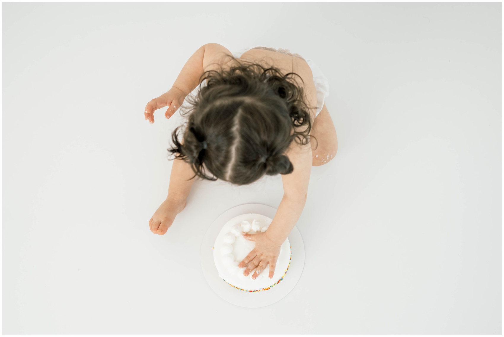 A look down at a baby girl pressing her hand into a birthday cake