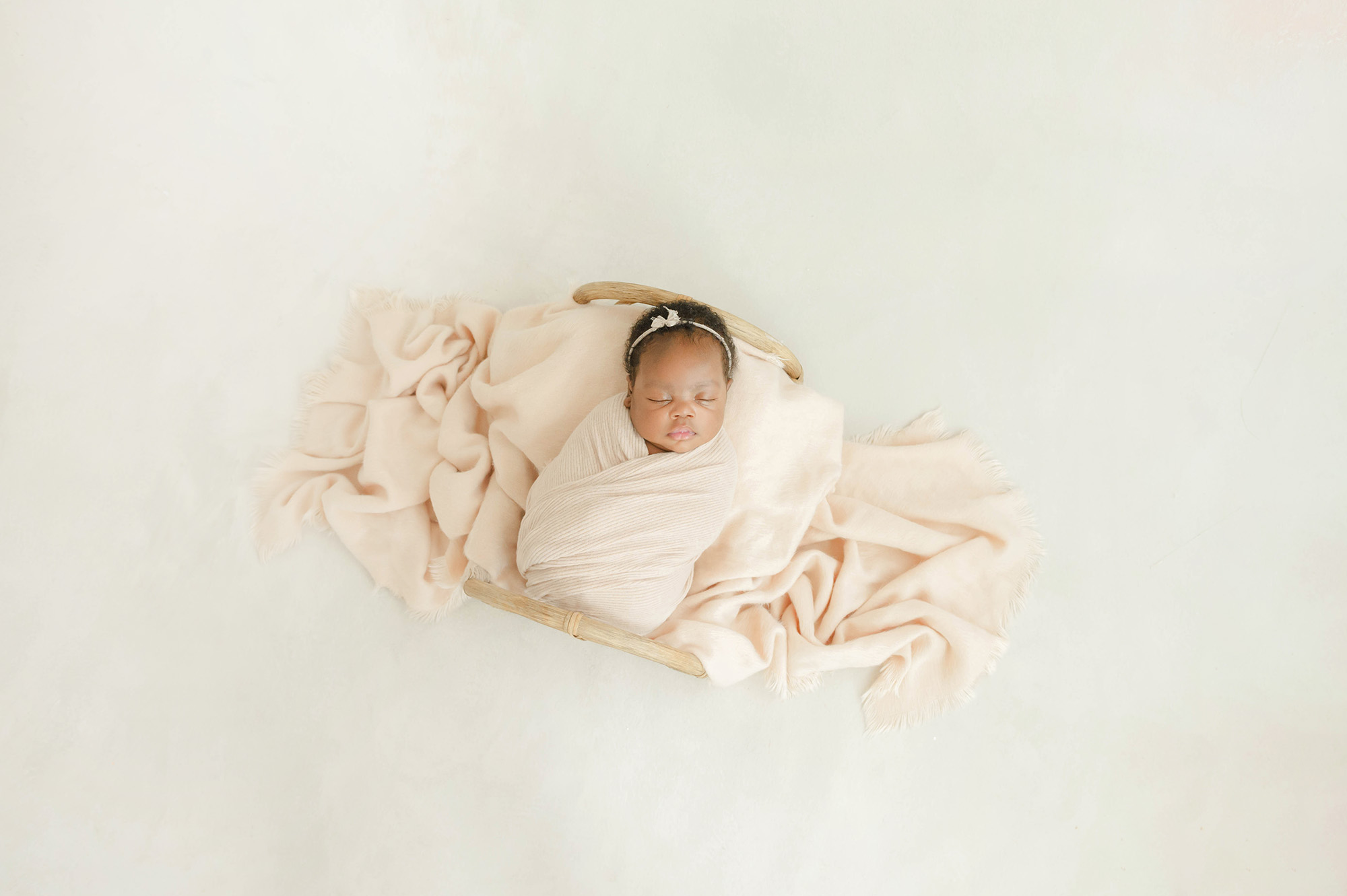 A newborn girl sleeps in a tiny wicker bed in a cream swaddle thanks to birthing classes in okc