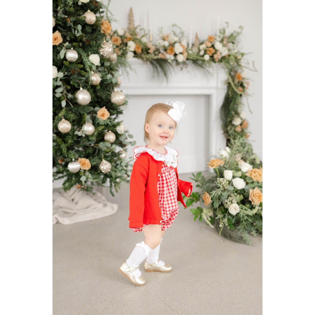 A baby girl in a red onesie explores a decorated studio