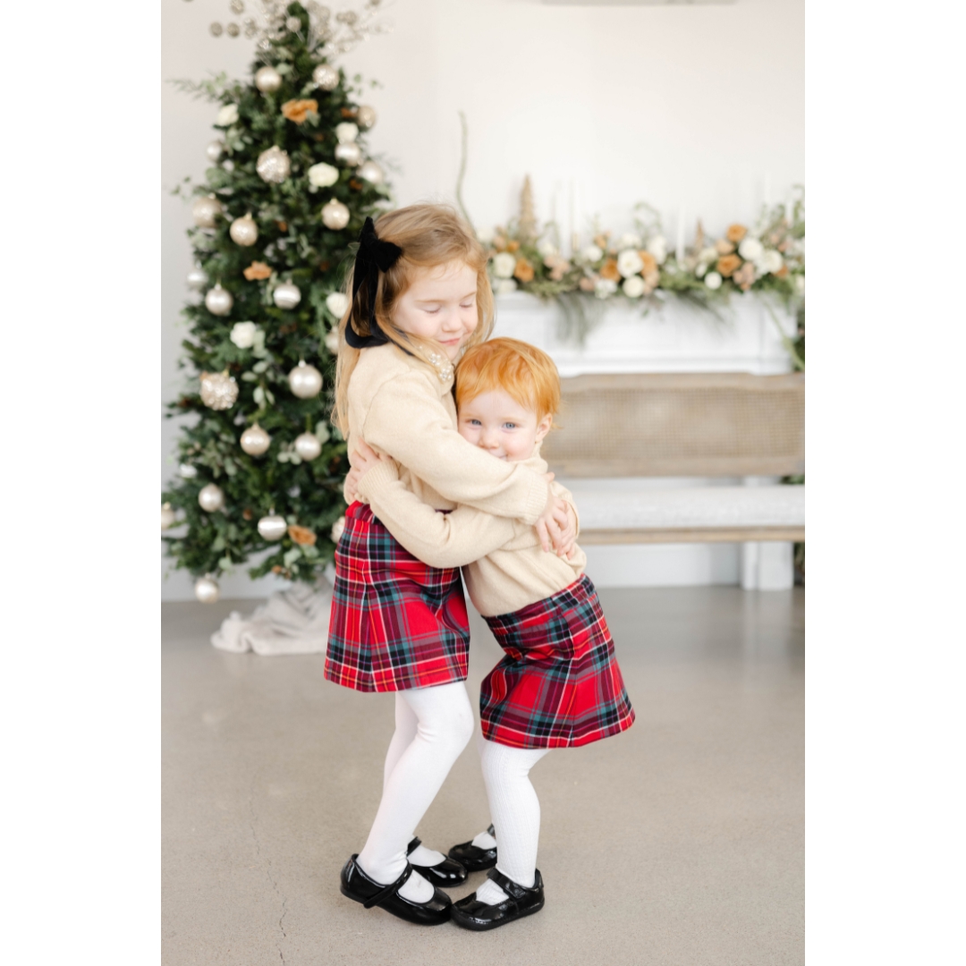 Happy toddler sisters hug with smiles in matching red skirts and tan sweaters in a studio before exploring christmas lights in okc