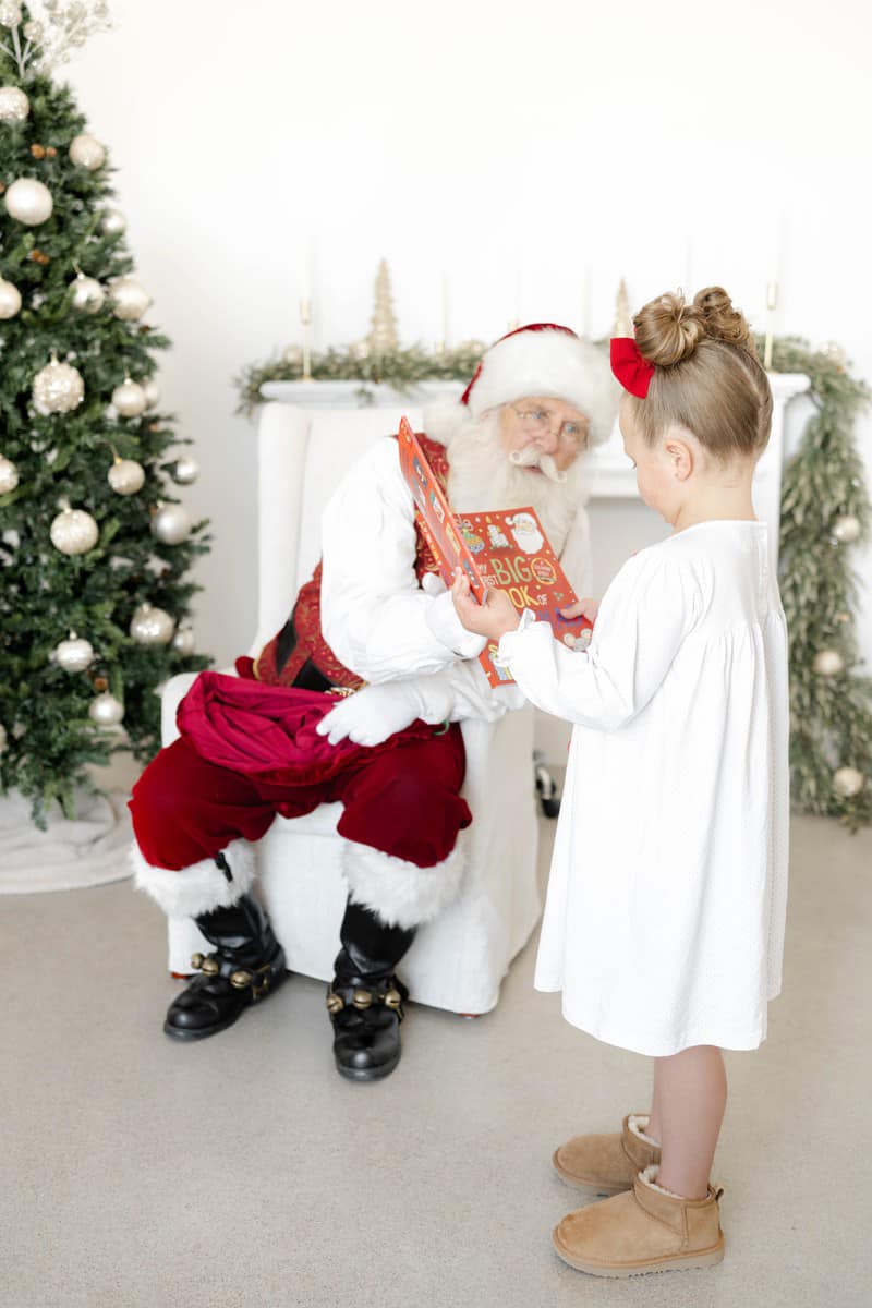 A young girl reads a book with santa in a white dress before going to see christmas lights in okc