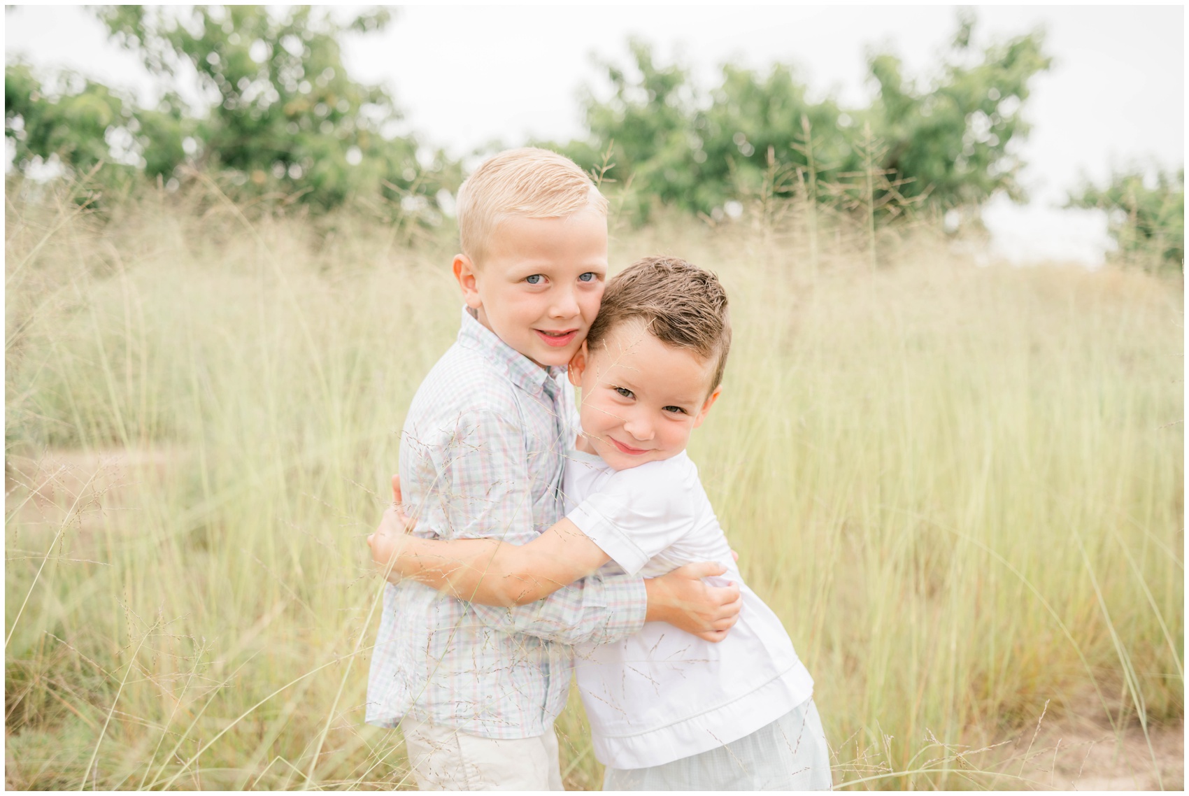 Happy toddler brothers hug in a field of tall grasses while smiling before visiting a corn maze in okc