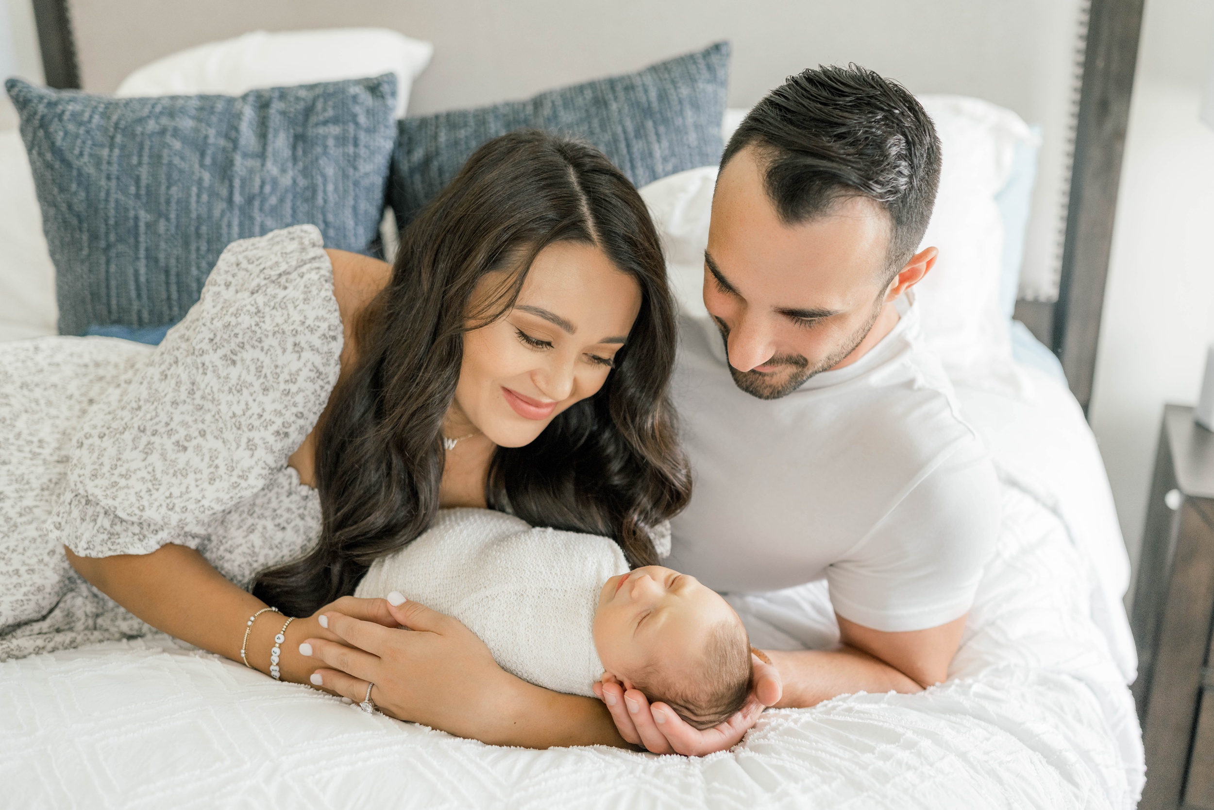 A happy mom snuggles her newborn baby with dad on a bed after visiting a day spa okc