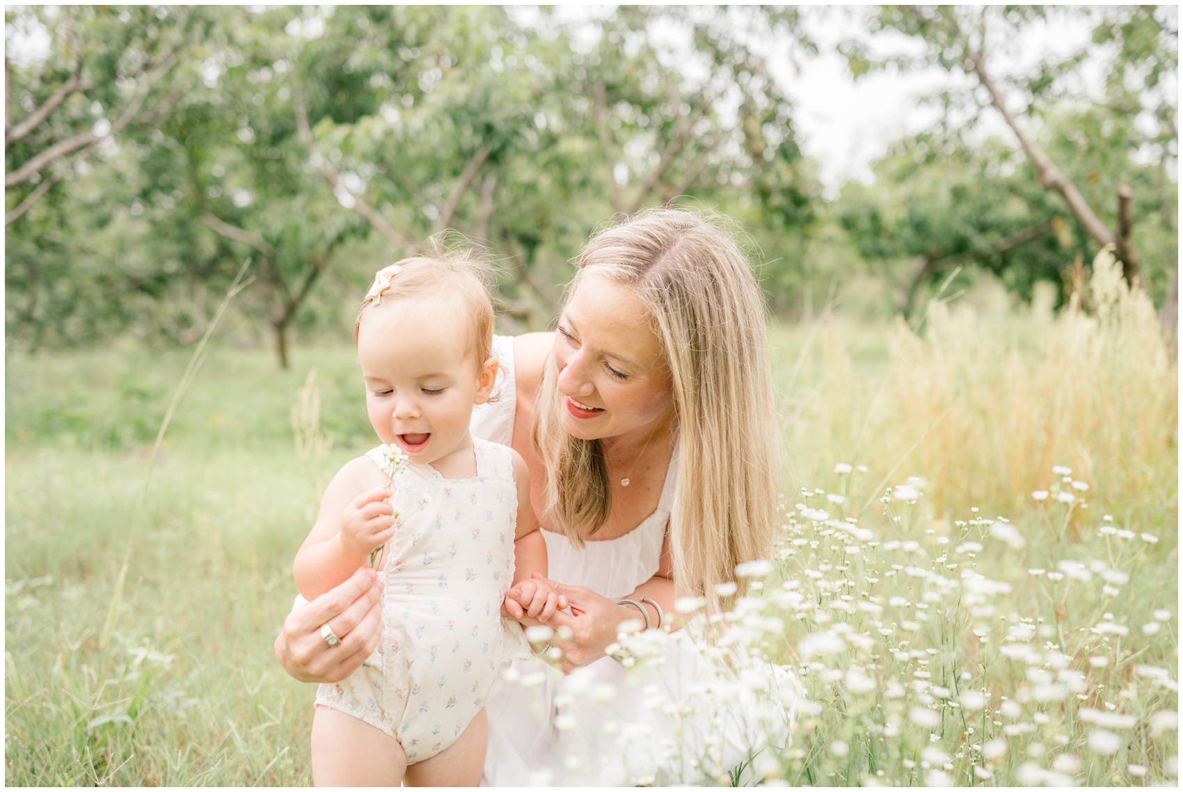 A baby in a onesie explores wildflowers with mom's help in a park before visiting fall festivals in okc