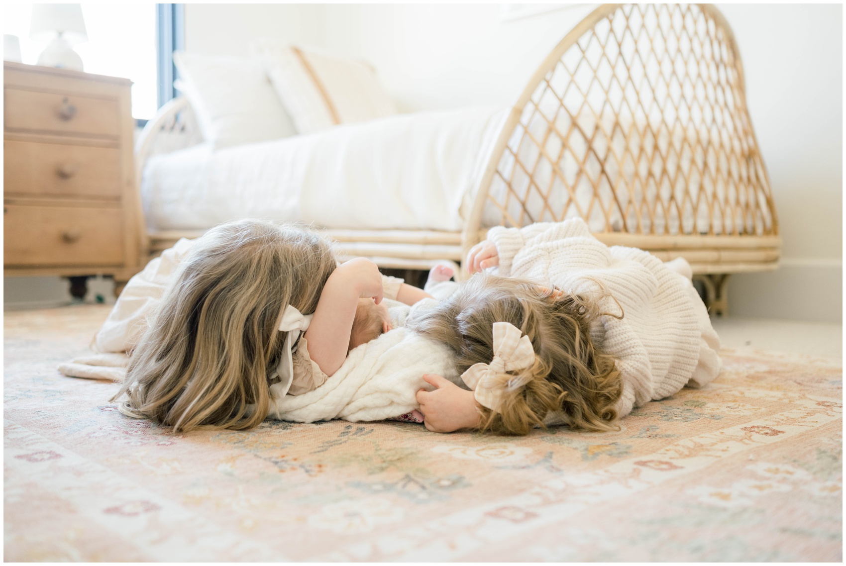 Two toddler sisters lay on the floor of a nursery cuddling their newborn sibling during family things to do in okc this weekend