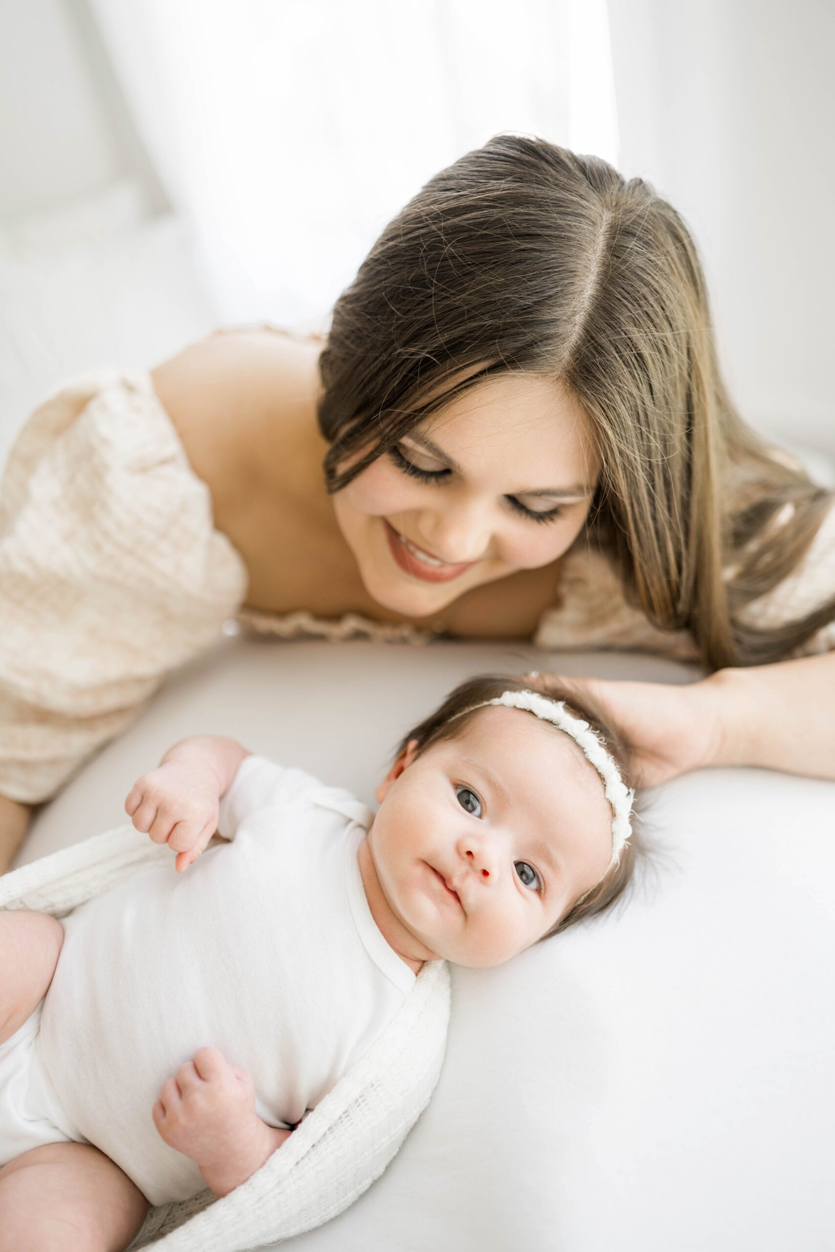 A mother lovingly looks down at her newborn daughter in a white shirt next to her