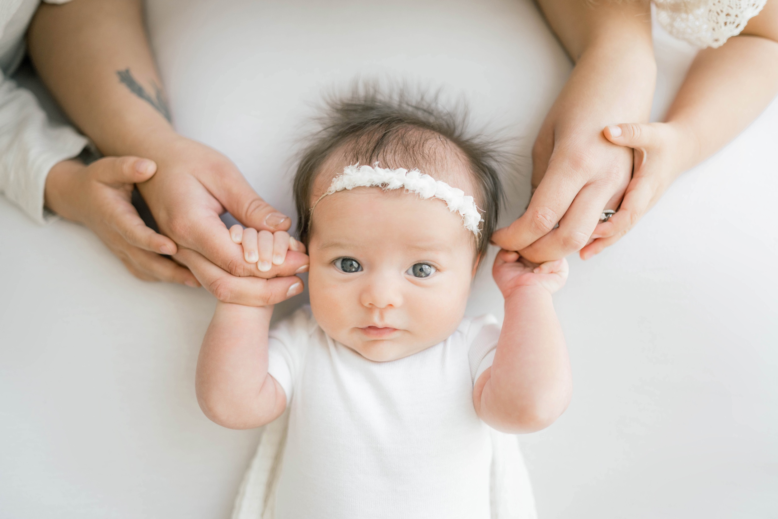 A newborn baby girl lays with eyes open holding mom and dad's fingers above her head after using holistic birthing services