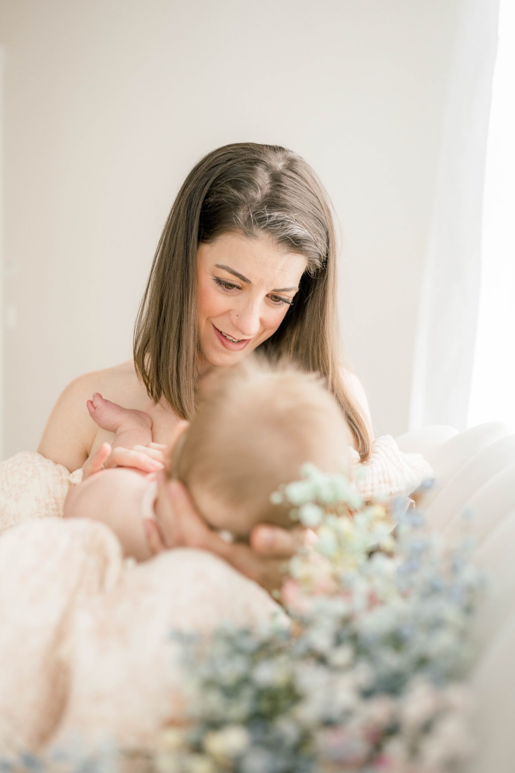 A happy mom holds her newborn baby in her lap while sitting across a couch before visiting kidoodles toy zone