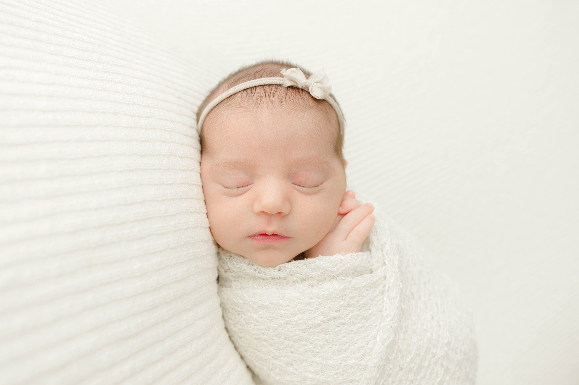 newborn girl wrapped in a white swaddle sleeping