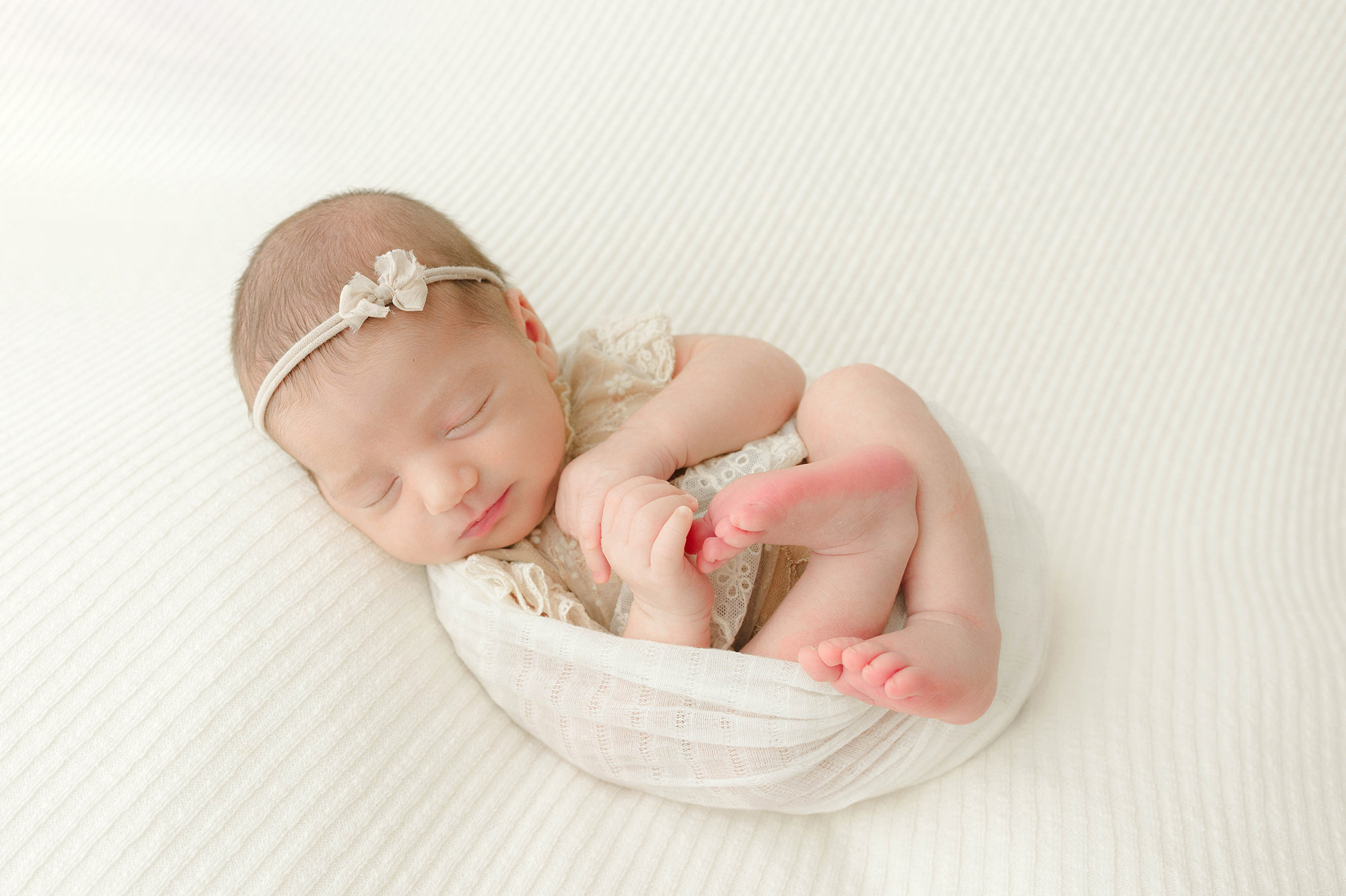 A newborn baby girl sleeps in a swaddle and yellow dress on a bed after meeting labor of love midwifery