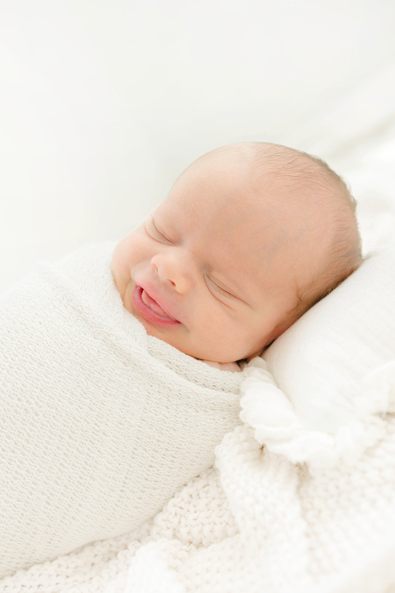 A newborn baby smiles in its sleep in a white swaddle thanks to okc birth center