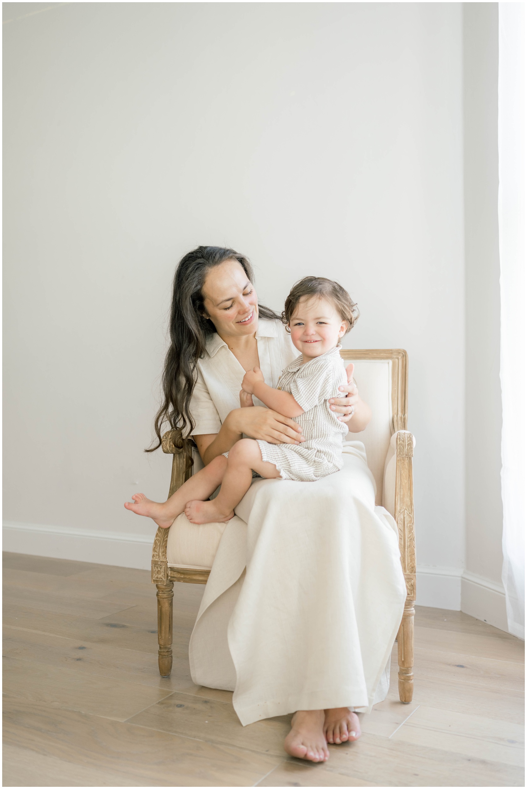 A happy toddler sits in mom's lap while smiling in a studio after visiting okc clothing stores