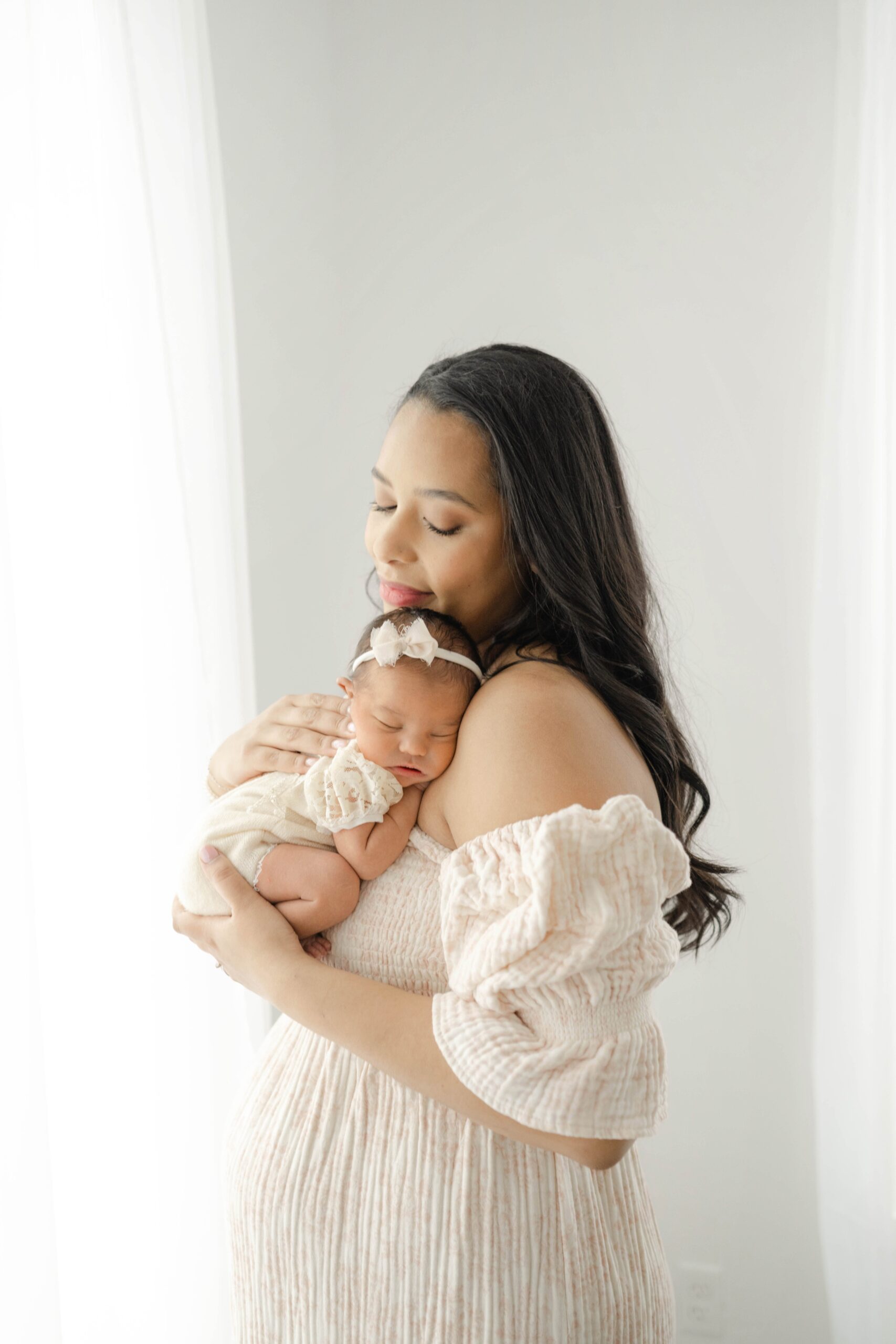 A happy new mom snuggles her sleeping newborn daughter against her chest while standing in a studio after leaving ou maternal fetal medicine