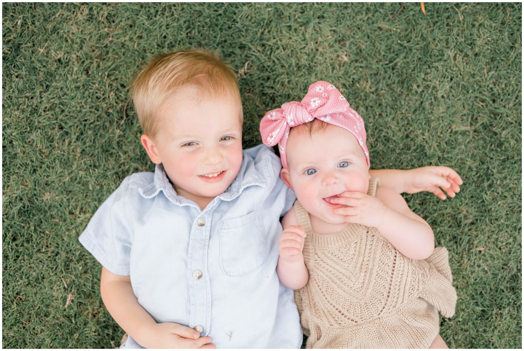 A young boy cuddles his baby sister while laying in a park lawn after visiting private preschools in okc