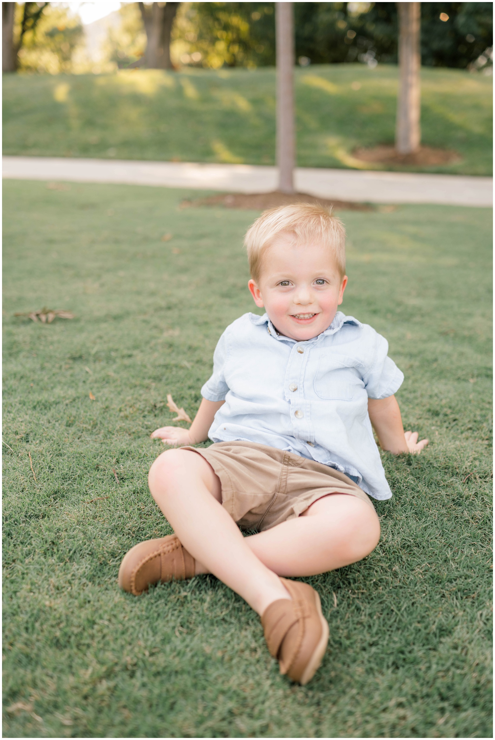 A young boy in a blue shirt leans back while sitting in a park lawn after finding private preschools in okc