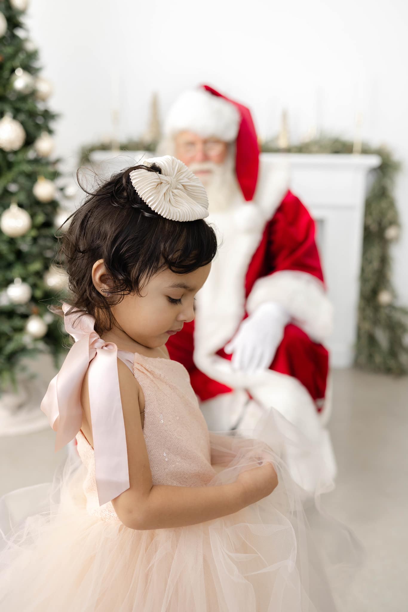 A young girl in a pink dress plays with her tule dress before meeting santa in okc sitting behind her