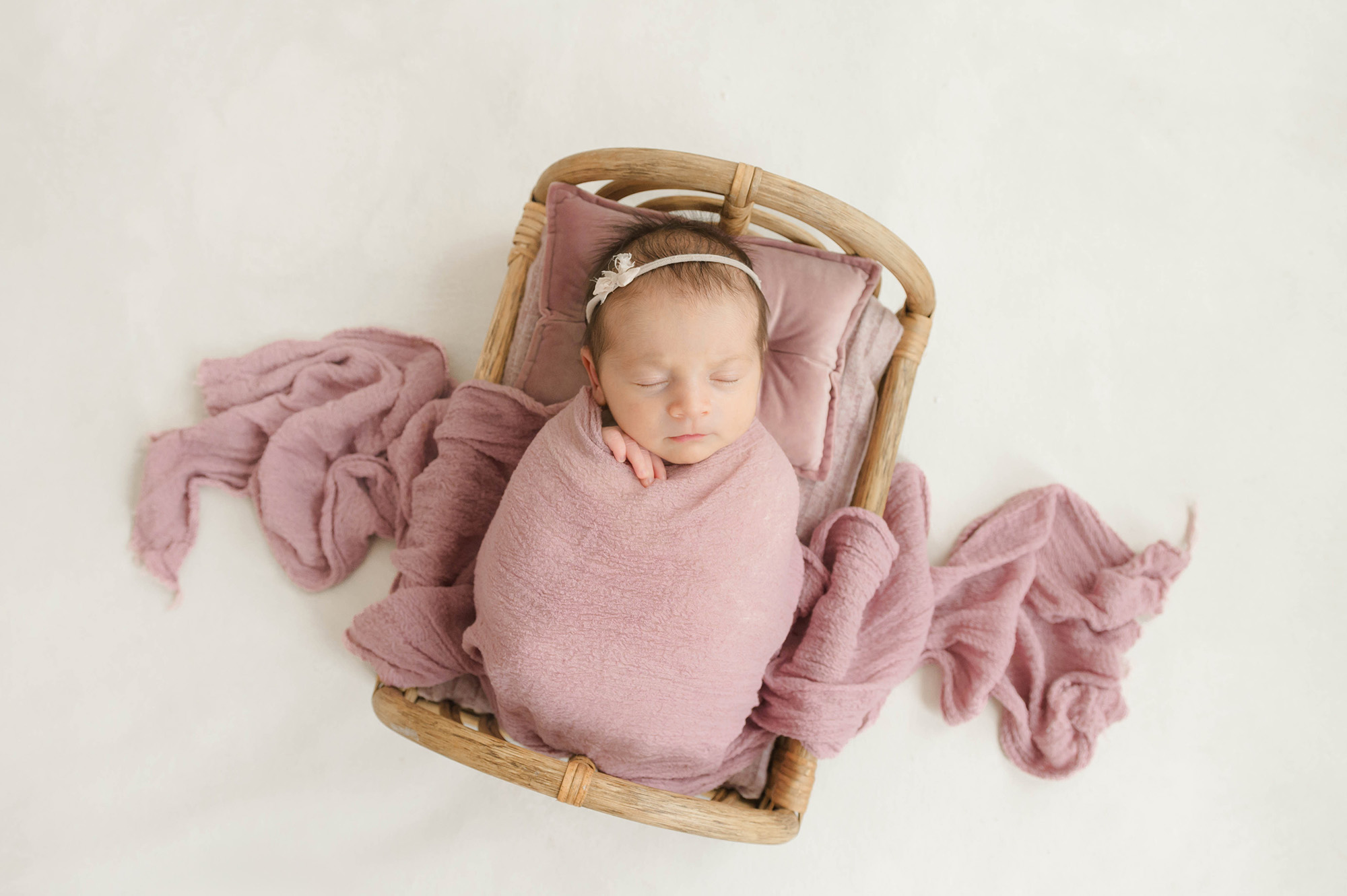 A newborn abby sleeps in a wicket crib in a pink swaddle