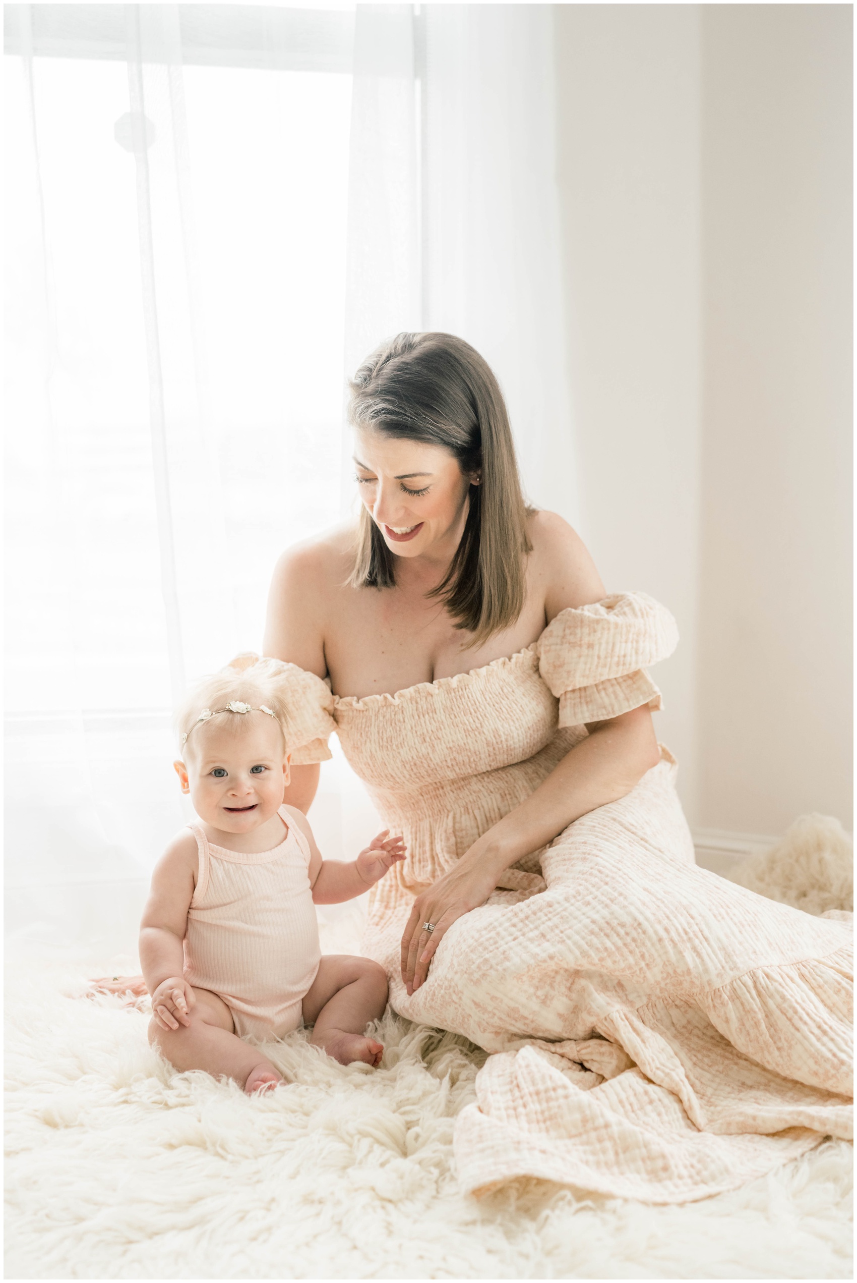 A baby girl sits on a rug playing with mom in a studio window before some swim lessons in okc