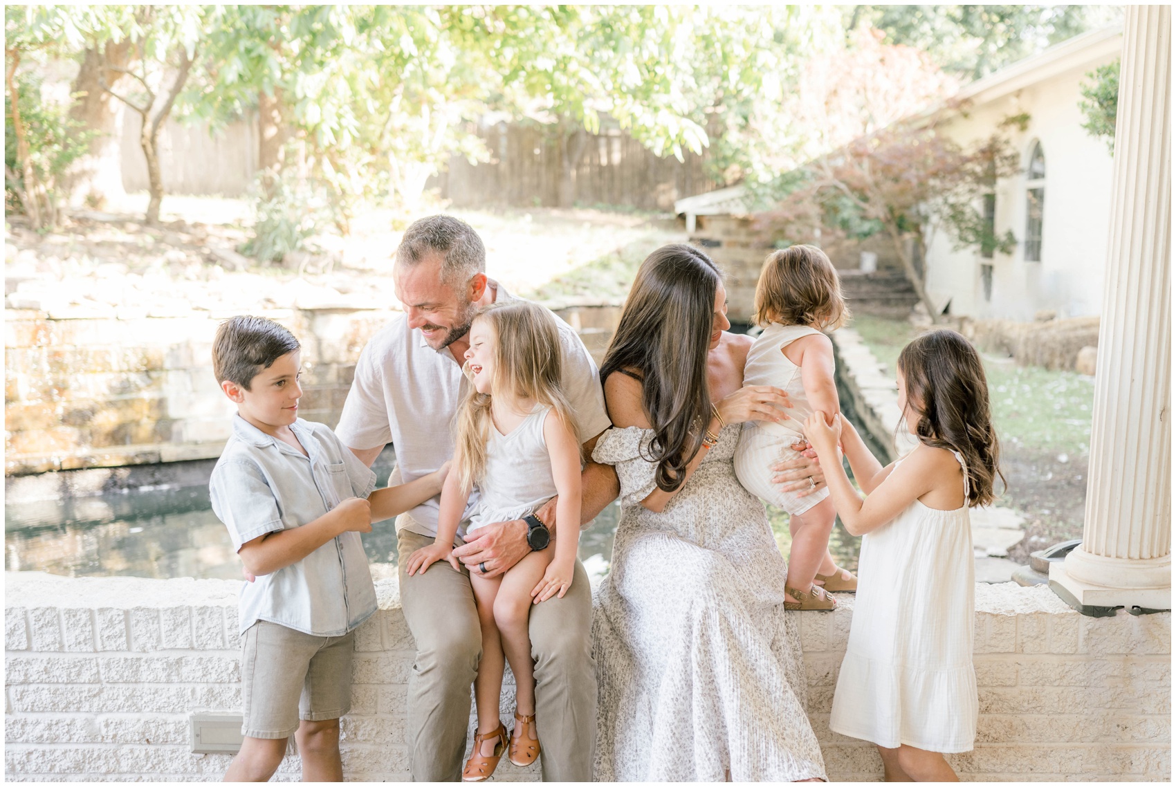 A mom and dad sit on a patio wall playing with their four young children