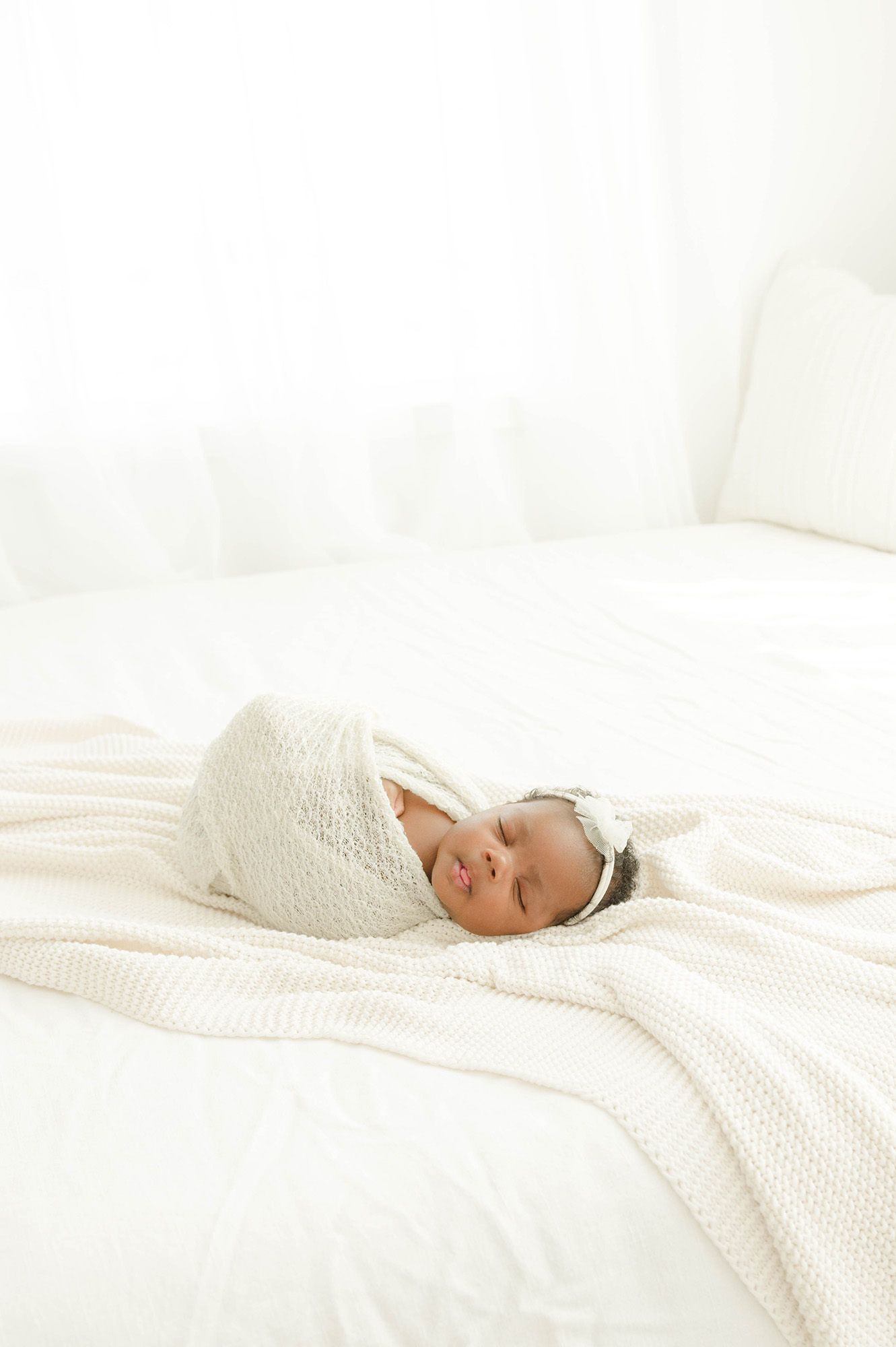 A newborn sleeps on a white bed in a matching swaddle with tongue out after visiting tin lizzie's okc