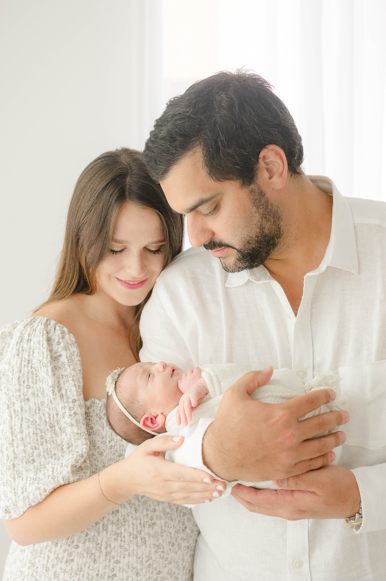 A newborn baby sleeps in dad's arms as mom leans on his shoulder