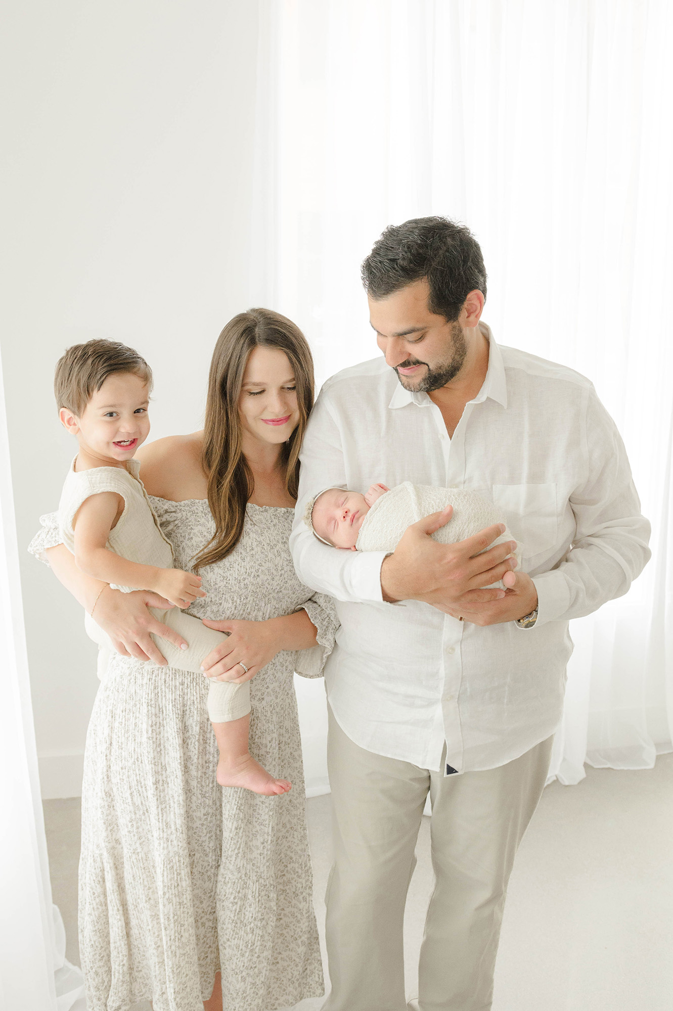 A mom and dad stand in a studio holding their toddler son and sleeping newborn before visiting tongue tie specialists in oklahoma city